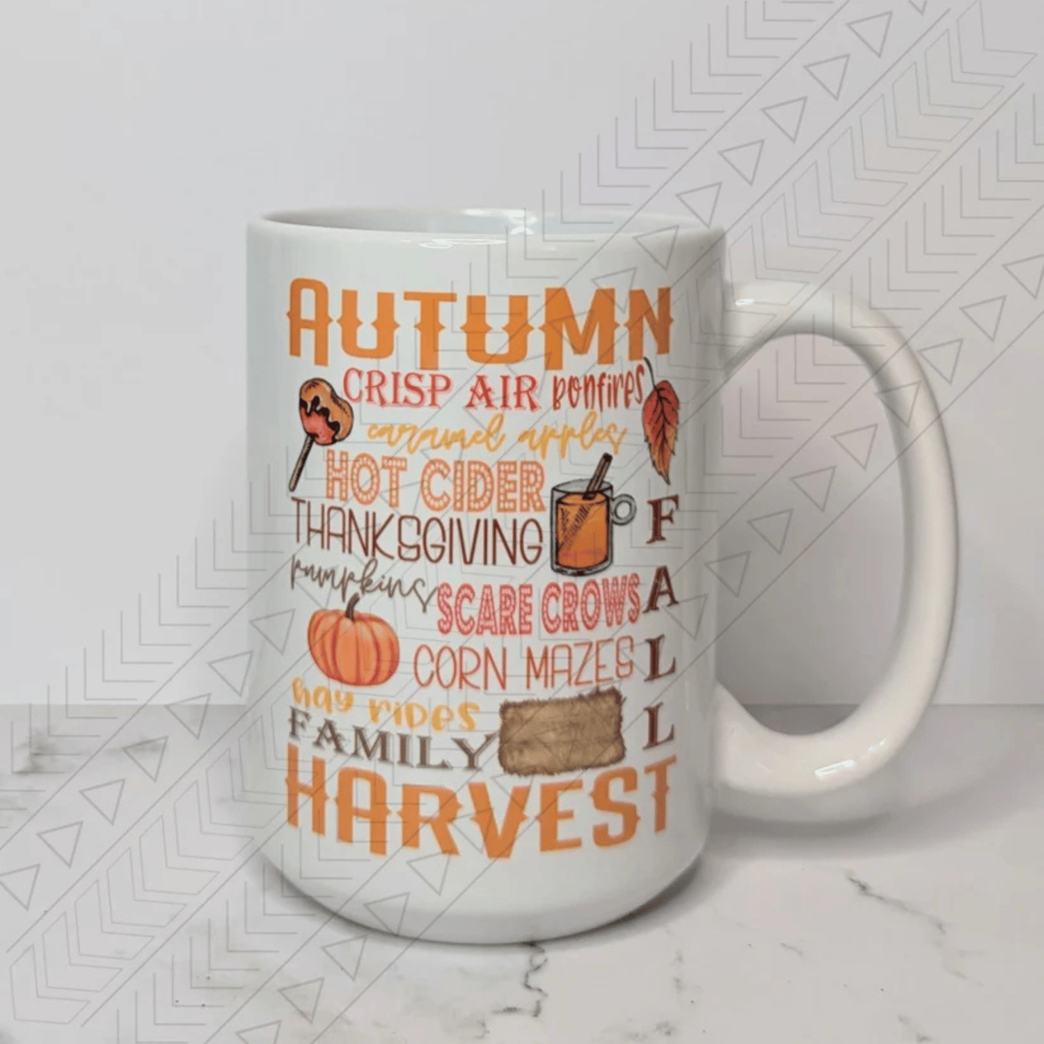 A white ceramic mug featuring a collage of autumn-themed words and images. The largest words are "AUTUMN" and "HARVEST" in orange and brown lettering. Other phrases include "CRISP AIR," "BONFIRES," "CARAMEL APPLES," "HOT CIDER," "THANKSGIVING," and more. 