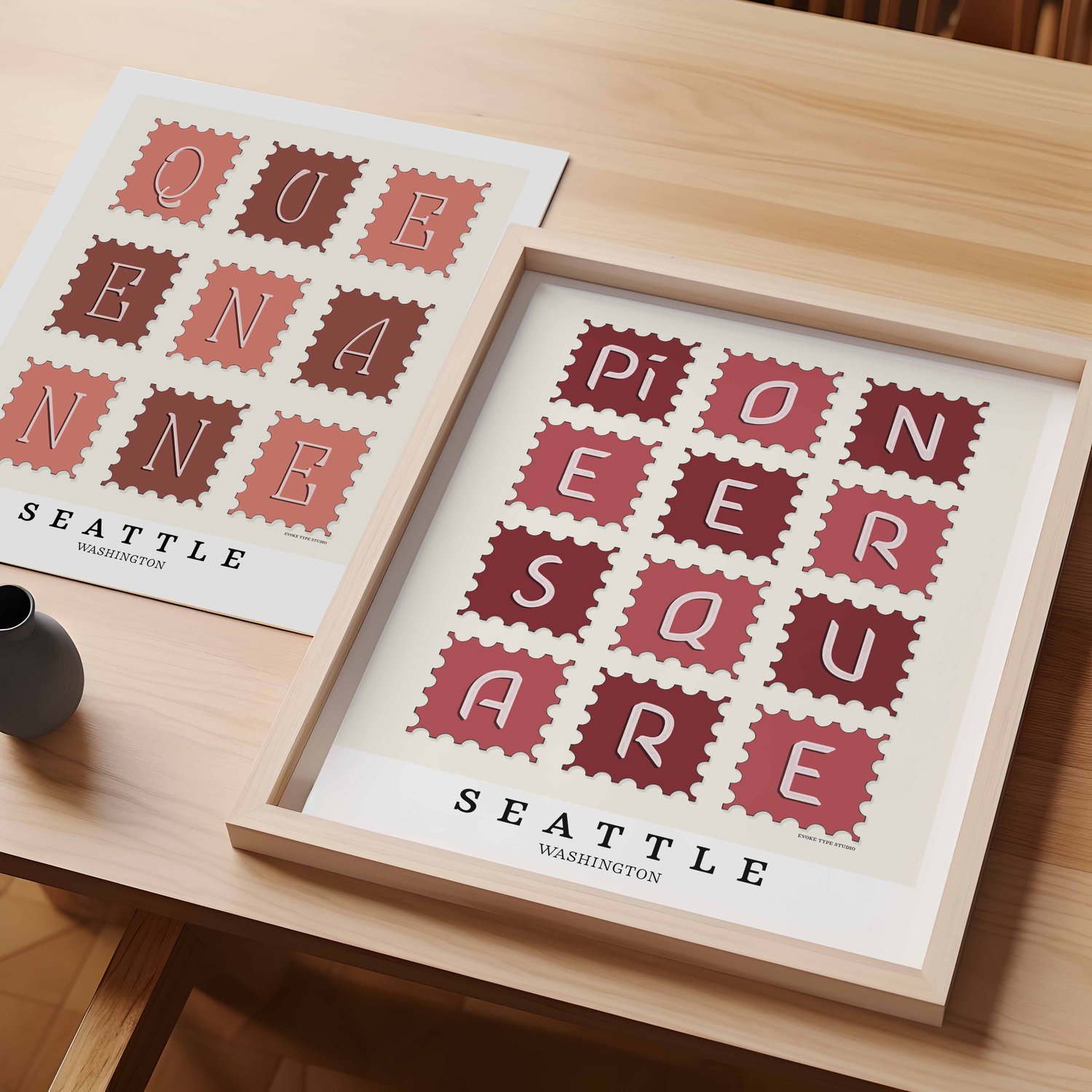 A table with an unframed artwork of Queen Anne postage stamp art and a framed artwork of Pioneer Square postage stamp art