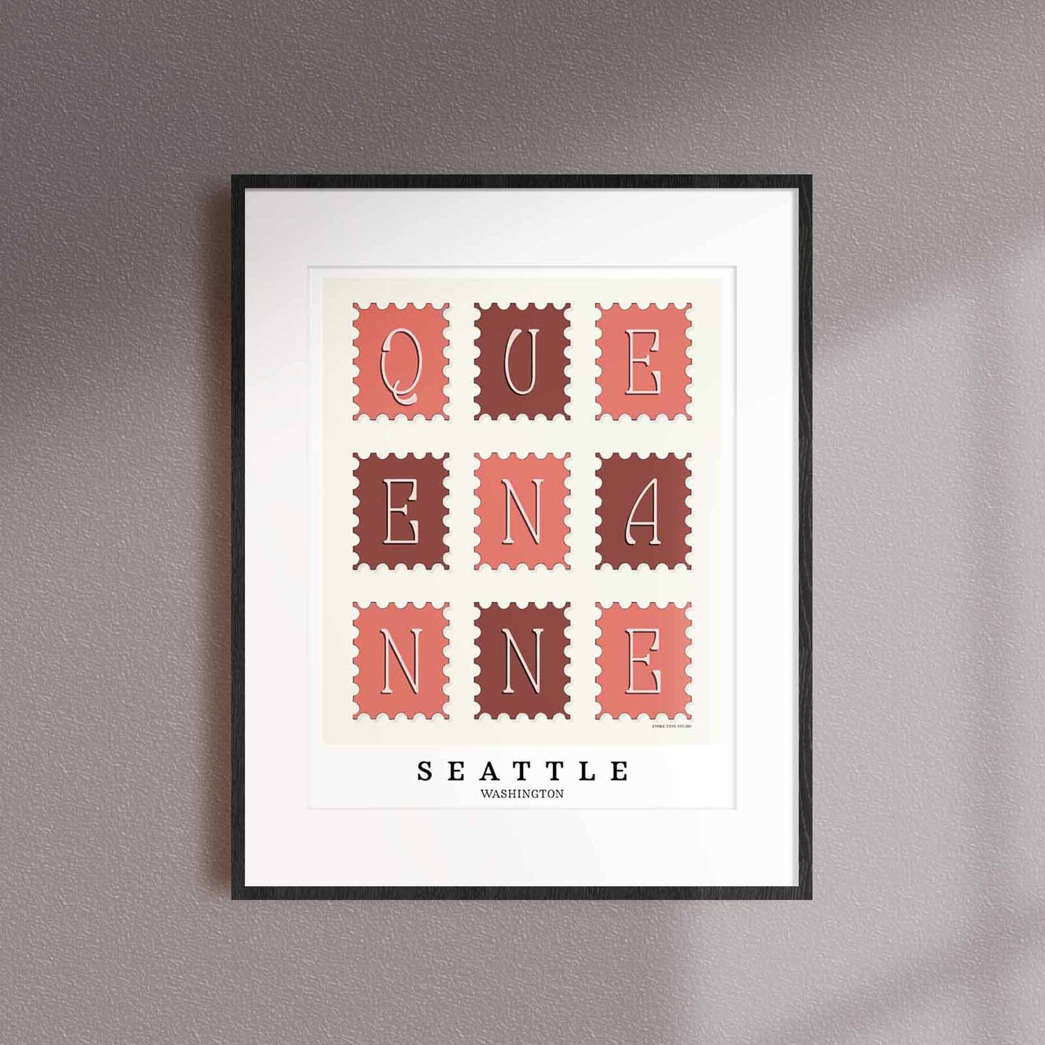 A framed picture of postage stamps featuring the Queen Anne neighborhood in Seattle, Washington drawn in a unique lettering style. Artwork has a pink, burgundy and white color scheme