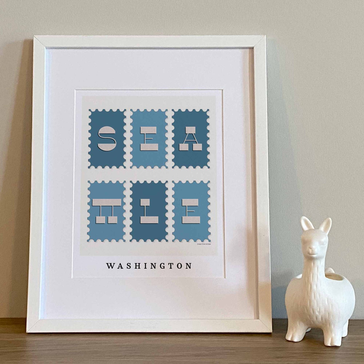 Hand-drawn Seattle postage stamp style wall art featuring bold reverse-contrast typography in blues and soft neutrals.