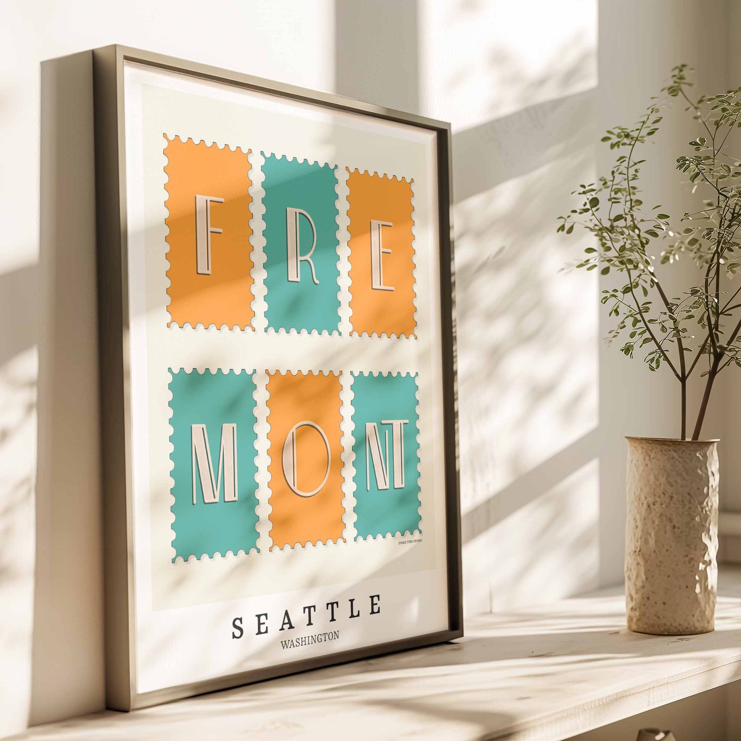 A framed picture of postage stamps featuring the Fremont neighborhood in Seattle, Washington drawn in a unique lettering style. Artwork has a bright blue and orange color scheme