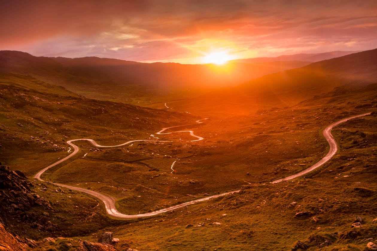 Winding mountain road on the Beara Peninsula in West Cork, Ireland, photographed at sunset with vivid orange light flooding the valley, illustrating how setting, light, and composition combine to create strong emotional impact in photography, featured in 