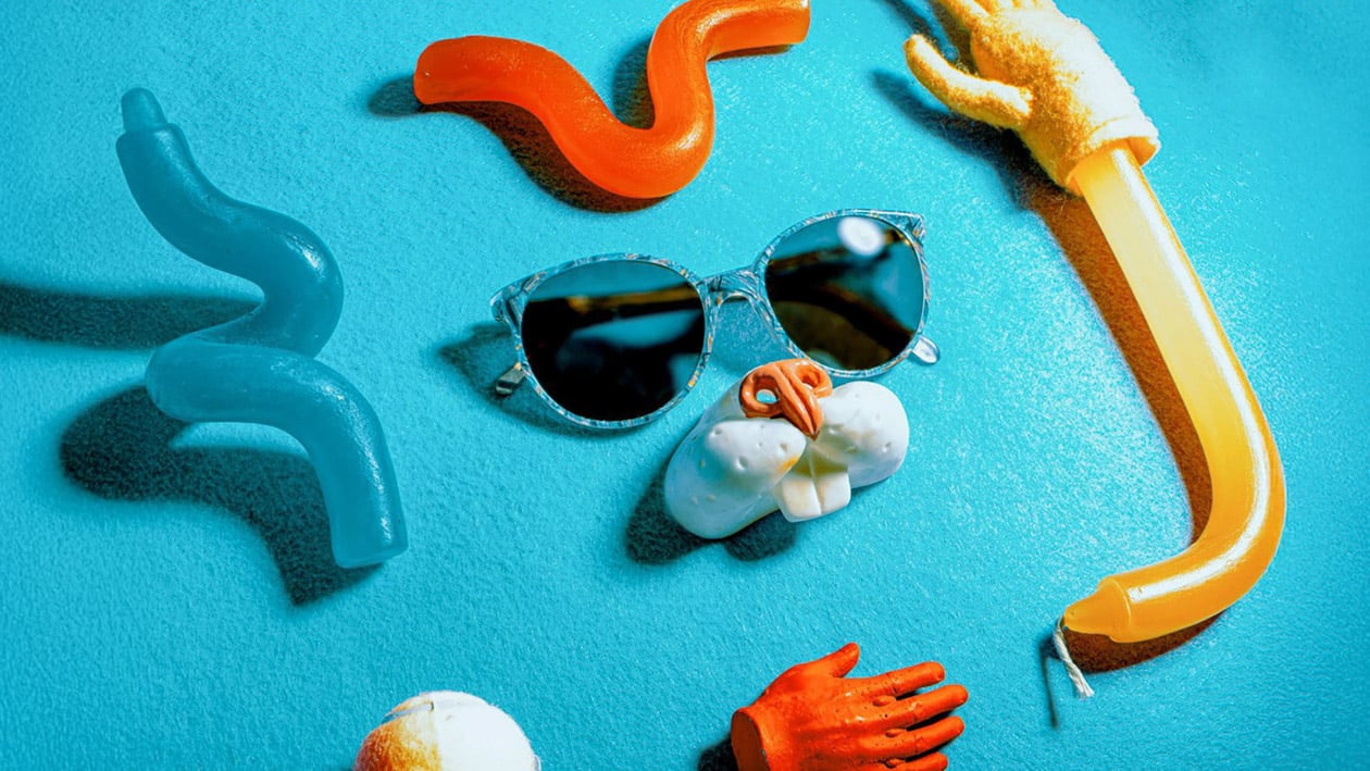 Flat lay of colorful objects arranged on a bright blue background, including sunglasses, plastic animal parts, and wavy shapes, creating a playful and imaginative face-like design — an example of how visual storytelling can shape brand identity, The Creat