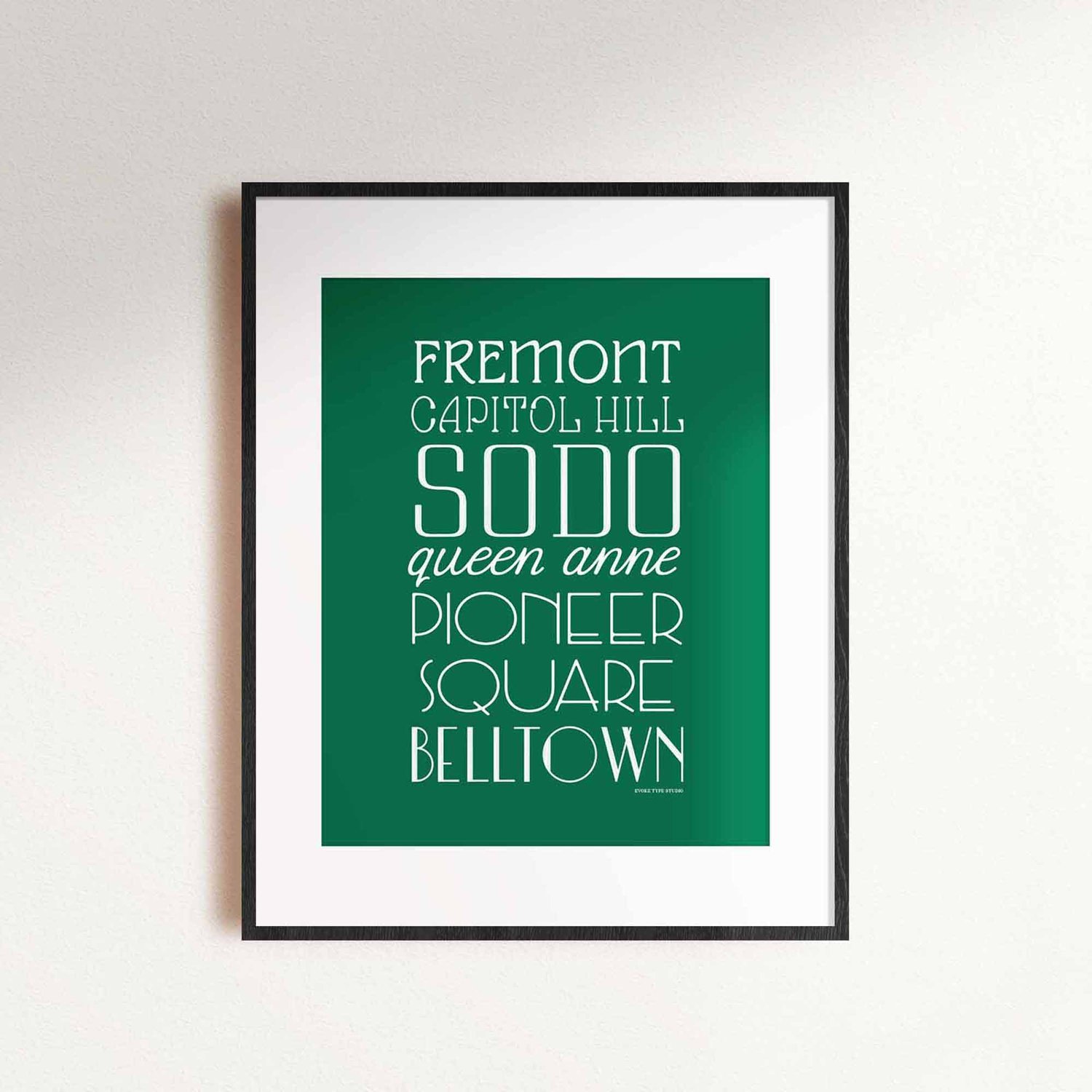 A framed picture of Seattle, Washington neighborhoods drawn in various lettering styles. Artwork has a green and white color scheme