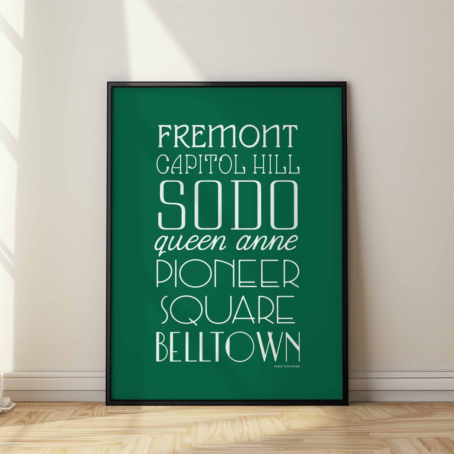 A framed picture of Seattle, Washington neighborhoods drawn in various lettering styles. Artwork has a green and white color scheme