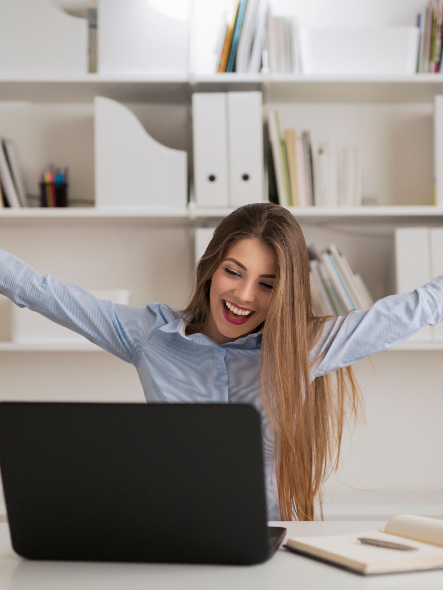 A young lady sitting in front of her computer celebrating that she was able to manage her finances in much less time than before
