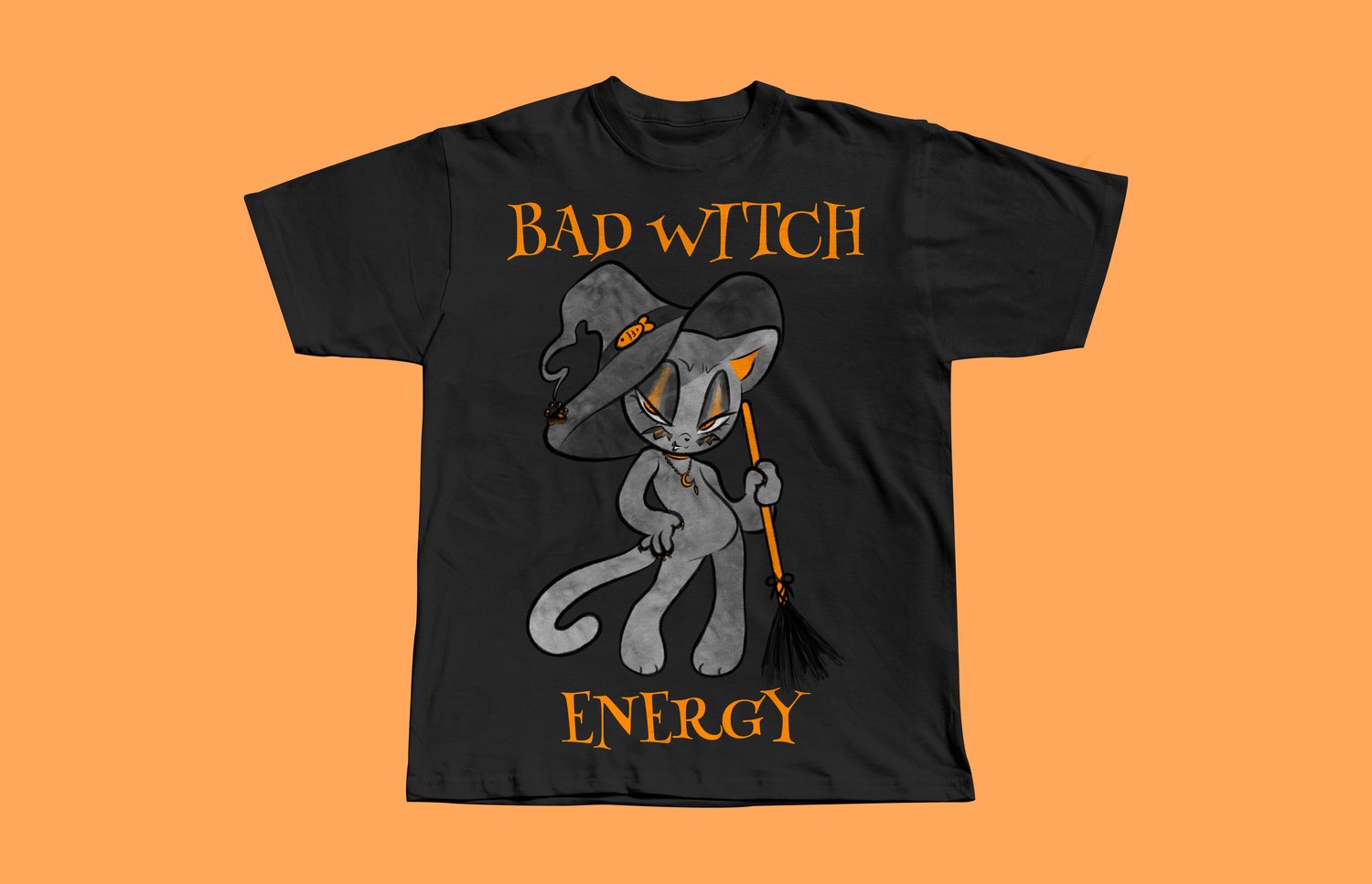 A black t-shirt on an orange background. Theres an illustration on the shirt of a black and orange cat in a witch hat holding an orange broom. Orange text reads "Bad Witch Energy."