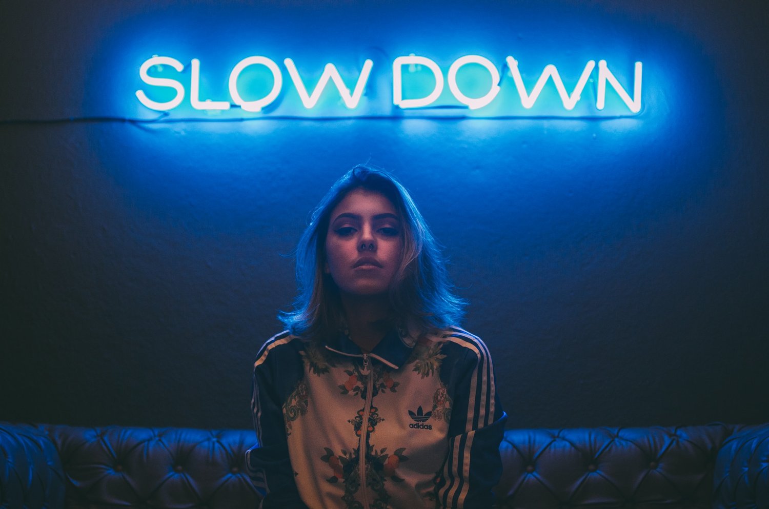 Blonde woman sitting on a couch with a blue glowing neon sign that says 