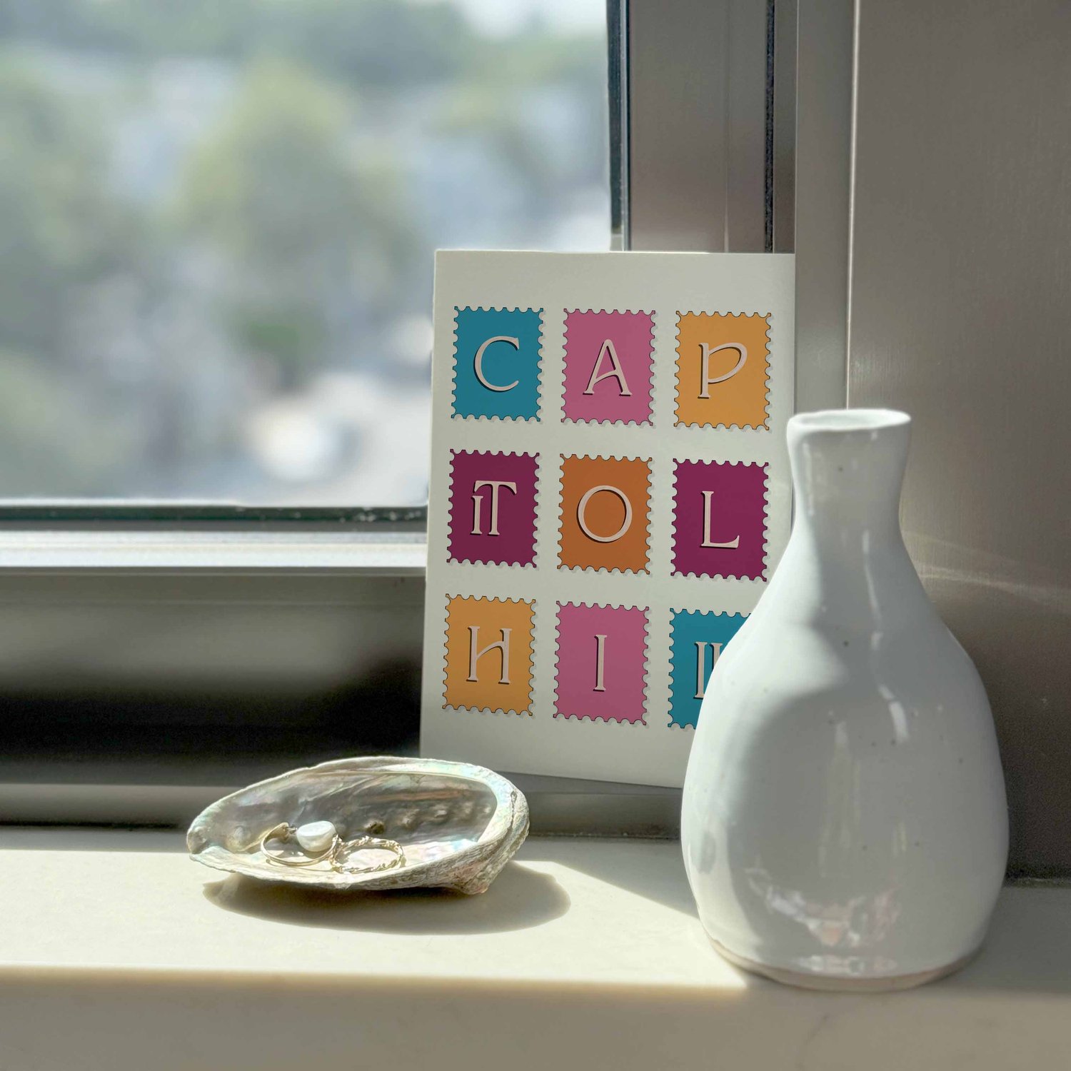 A typography-driven notecard that spells out Capitol Hill on various postage stamps, placed on a windowsill.