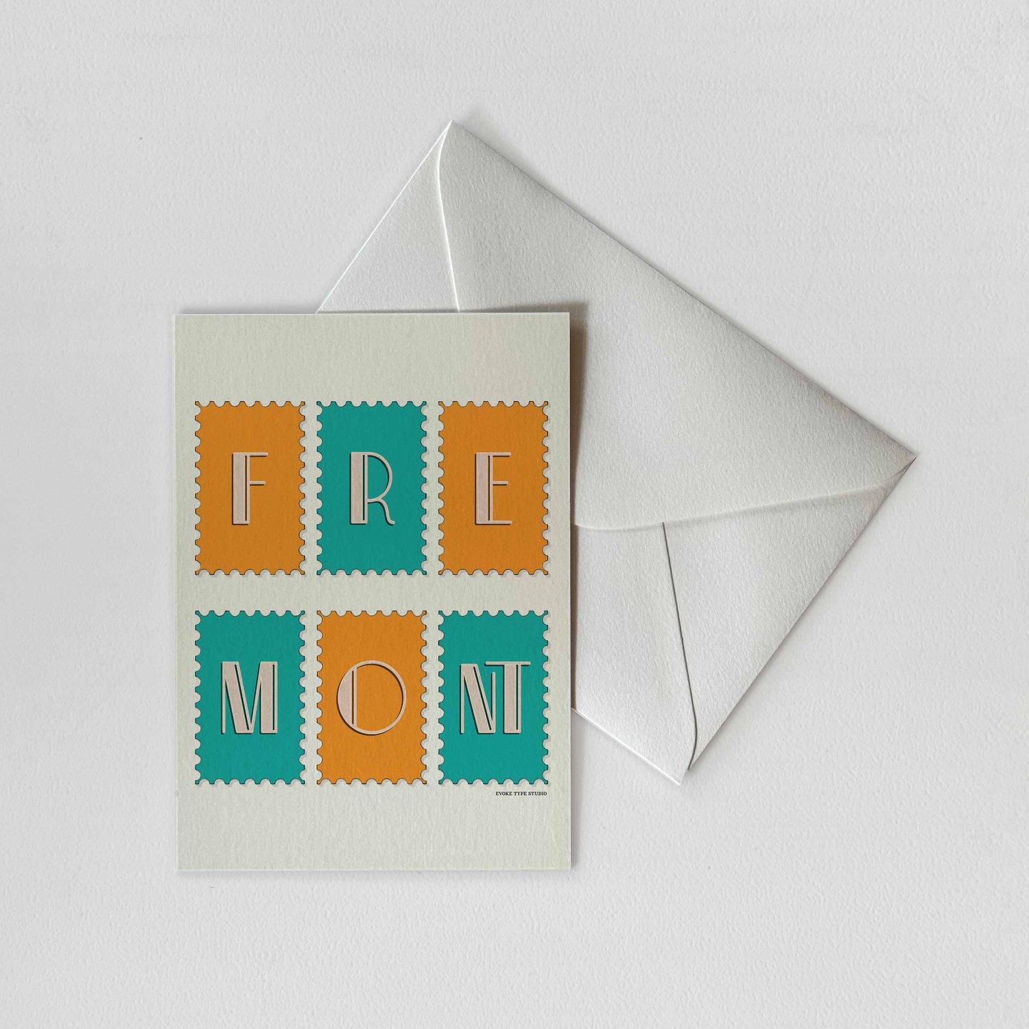 A notecard of postage stamps featuring the Fremont neighborhood in Seattle, Washington drawn in a unique lettering style with a white envelope. Artwork has a blue and orange color scheme