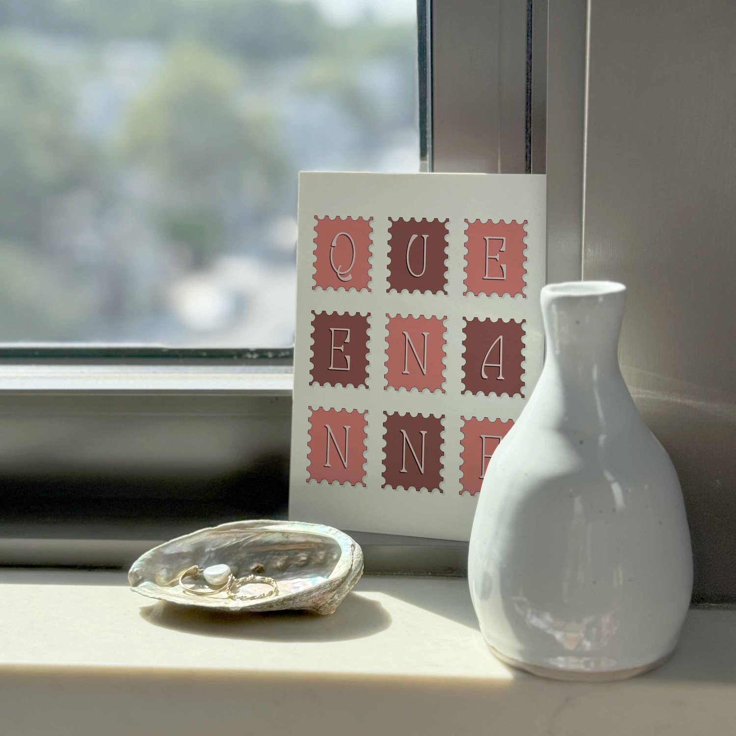 A typography-driven notecard that spells out 'Queen Anne' on various postage stamps, placed on a windowsill.