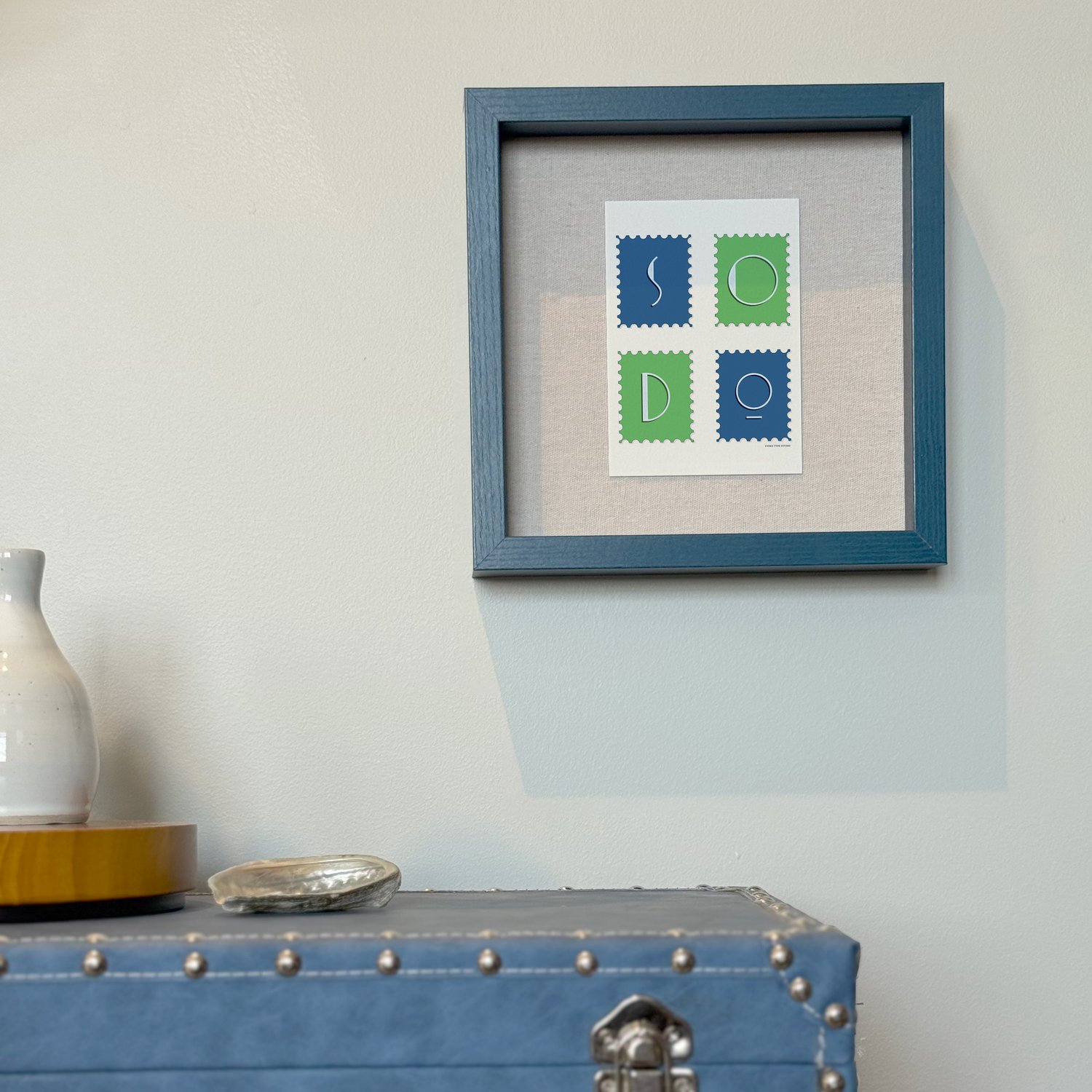A framed notecard in a shadow box hung on the wall with decorative items placed nearby.