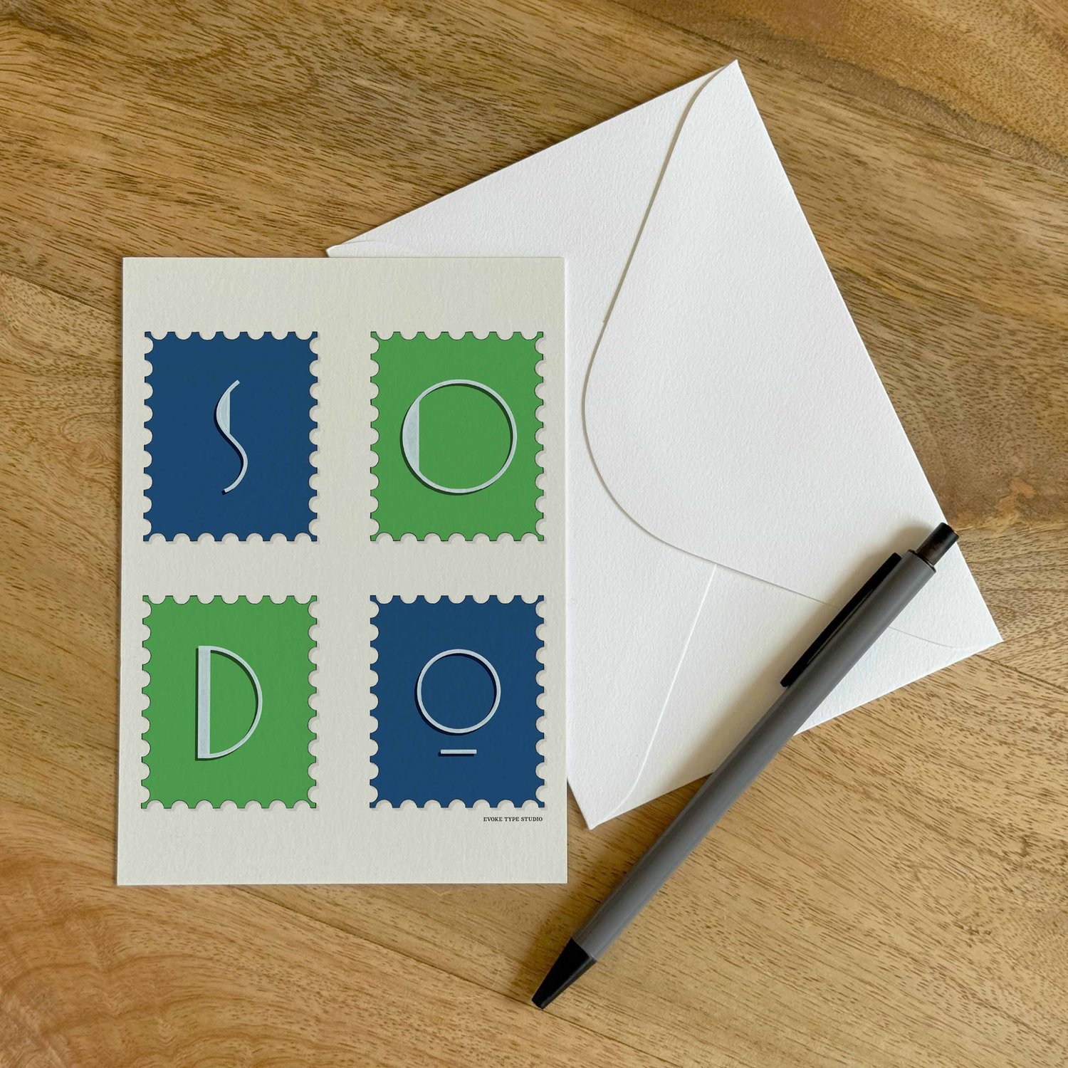 A colorful notecard sitting on a table with a white envelope and pen.