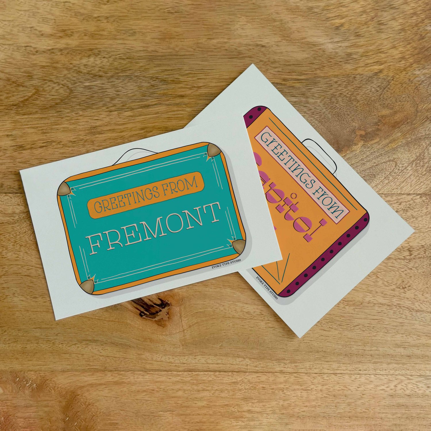 Two postcards, one placed on top of the other. Both postcards feature vintage suitcase illustrations and are for the Seattle, Washington area.