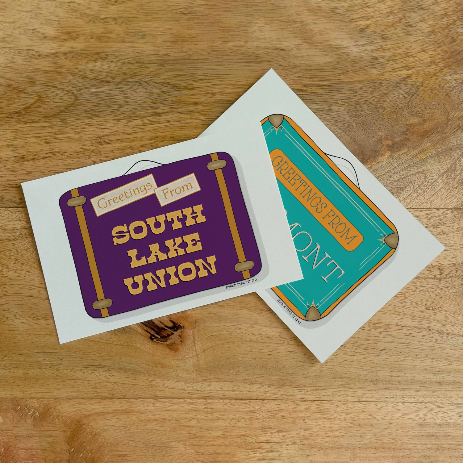 Two postcards, one placed on top of the other. Both postcards feature vintage suitcase illustrations and are for the Seattle, Washington area.