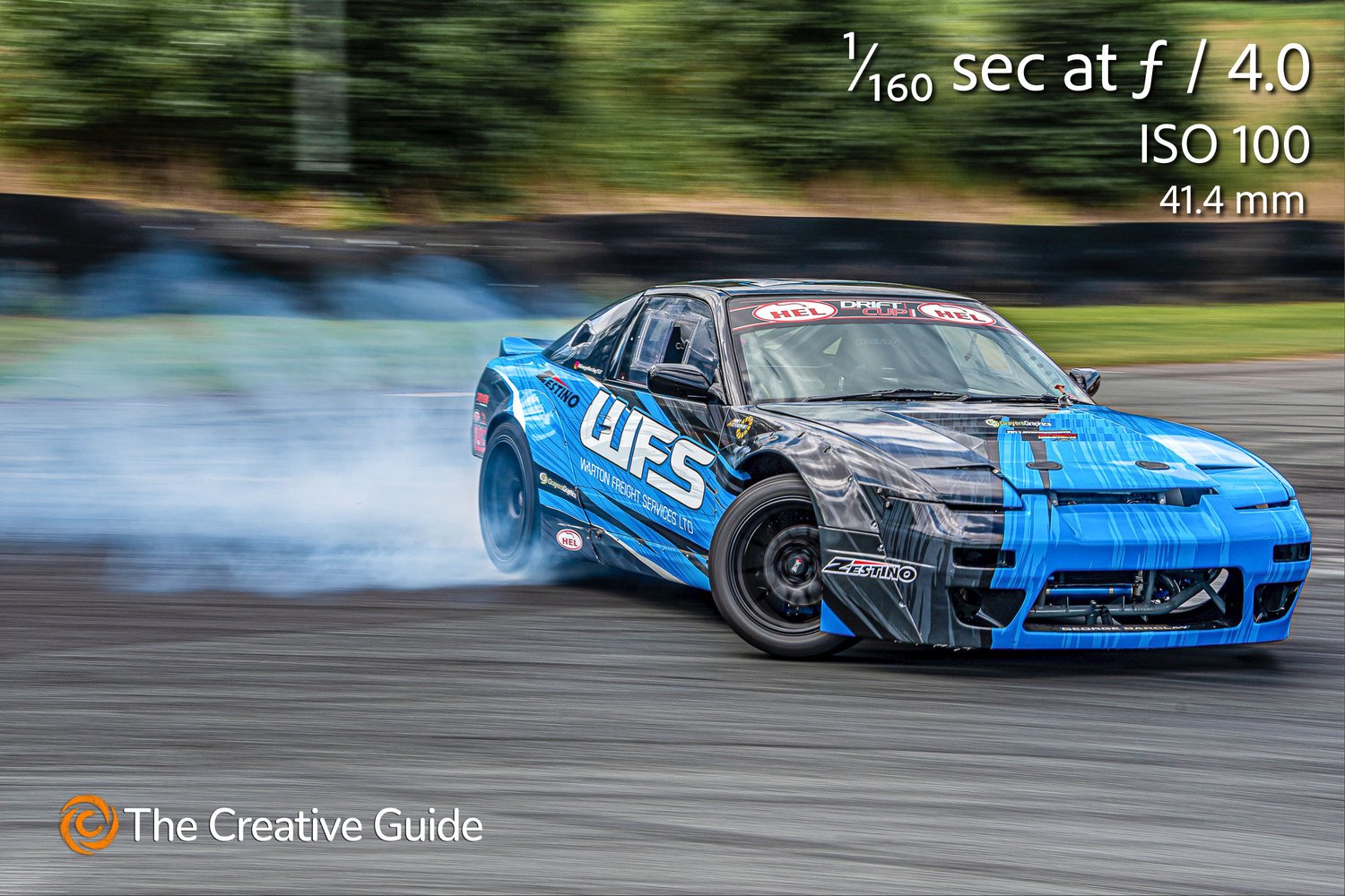 Racing car drifting on track, smoke from tires and blurred background emphasizing speed, photographed at 1/160 sec f/4 ISO 100, 41.4 mm, The Creative Guide Photo Gallery.