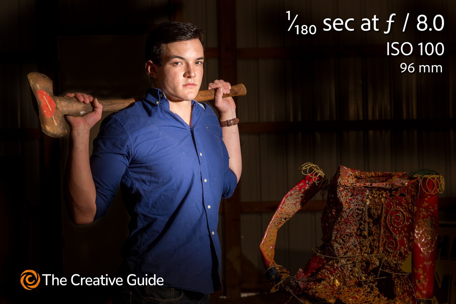 tudio-style portrait of young man in blue shirt holding a large sledgehammer over his shoulders, photographed at 1/180 sec f/8 ISO 100, 96 mm, The Creative Guide Photo Gallery.