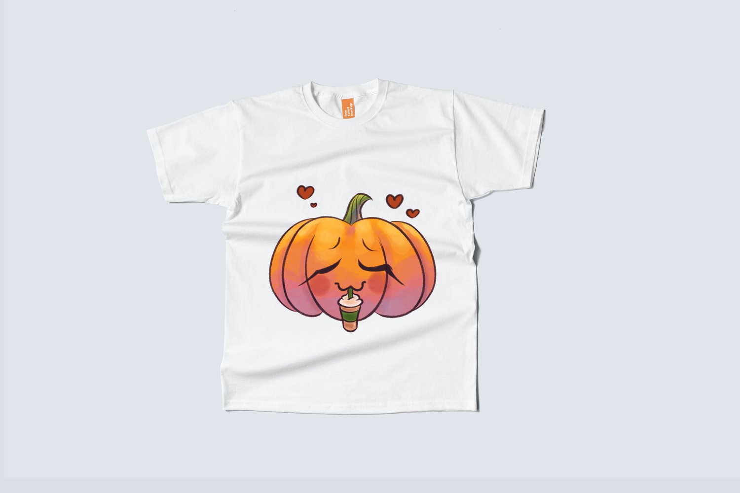 A white T-shirt on a pale, blue background. There is a cartoony, watercolour illustration of a jack-o-lantern drinking a pumpkin spice frappe on the shirt. Hearts are floating above the pumpkin.