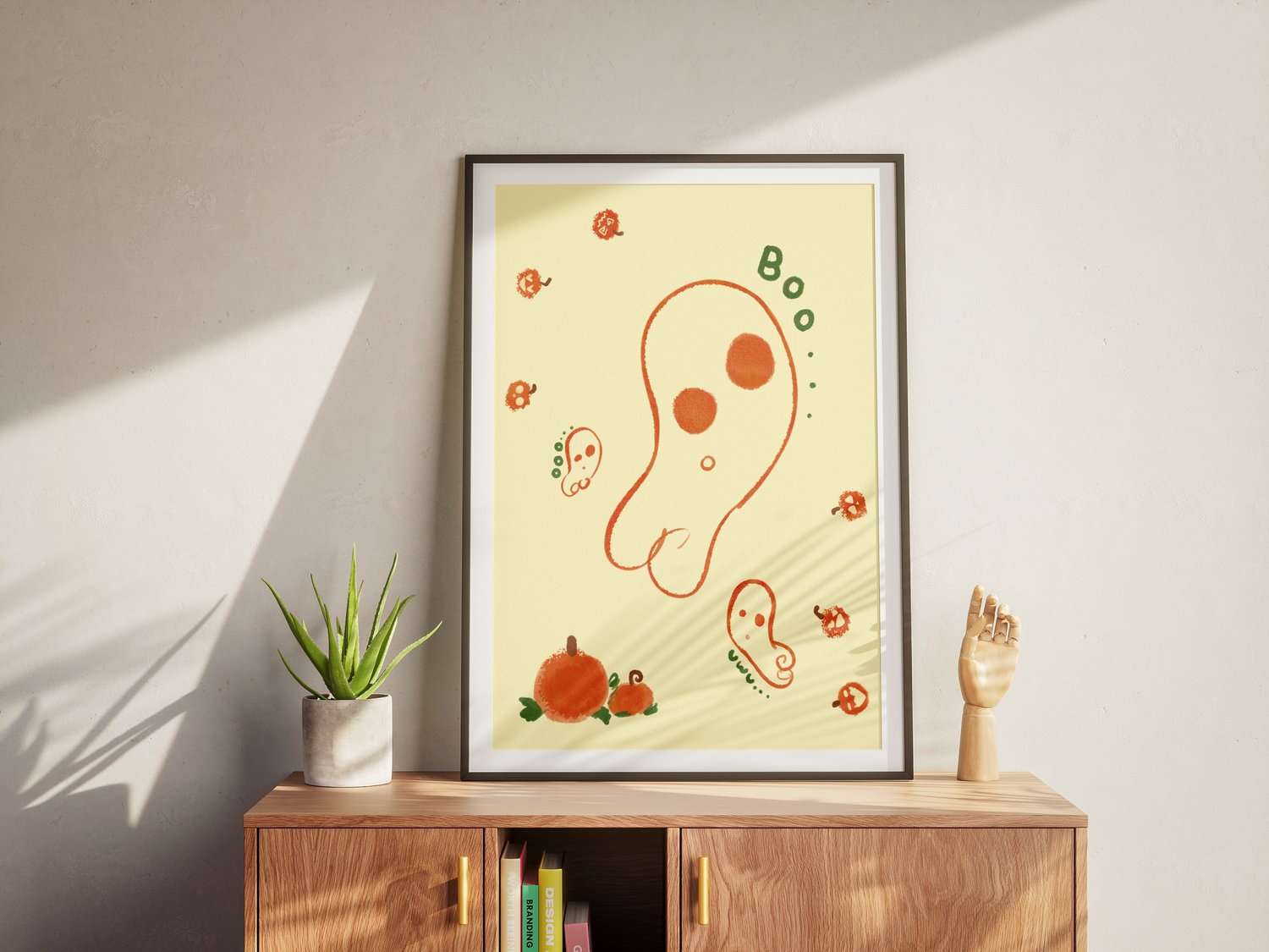 An art print of an abstract, wobbly ghost drawn in orange line art floats against a yellow background. Several smaller ghosts flank the biggest one. Small, abstract Jack-o-lanterns hop around the canvas happily. Two big orange pumpkins with green leaves a