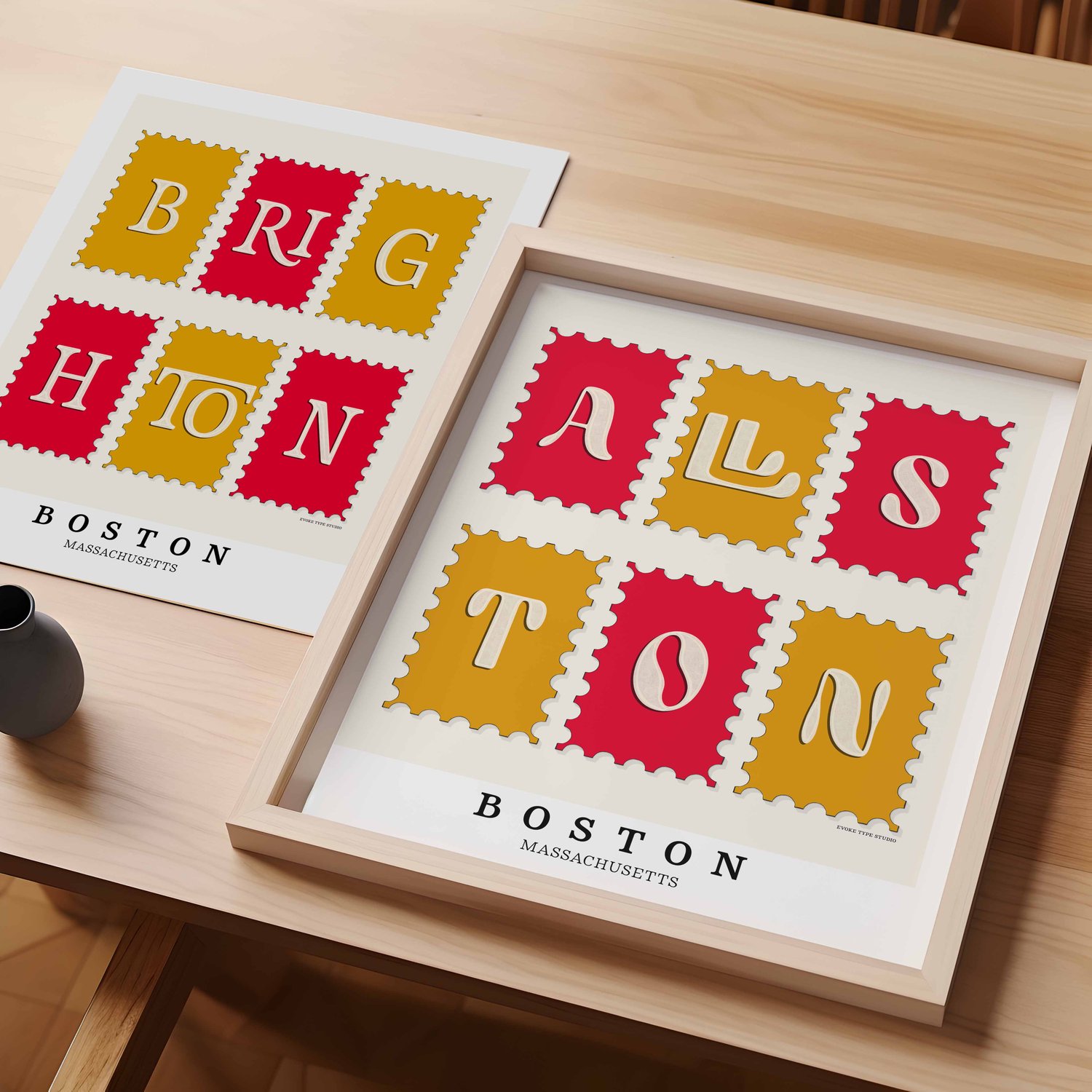 A table with an unframed artwork of Brighton postage stamp art and a framed artwork of Allston postage stamp art