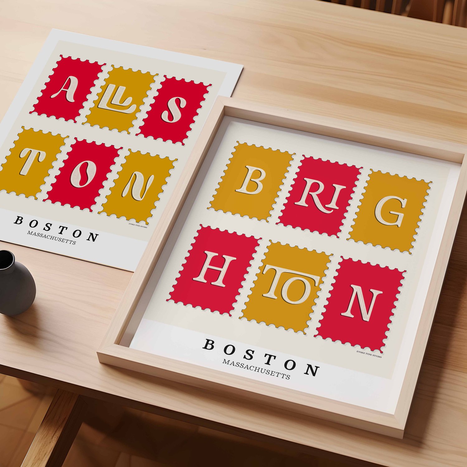A table with an unframed artwork of Allston postage stamp art and a framed artwork of Brighton postage stamp art