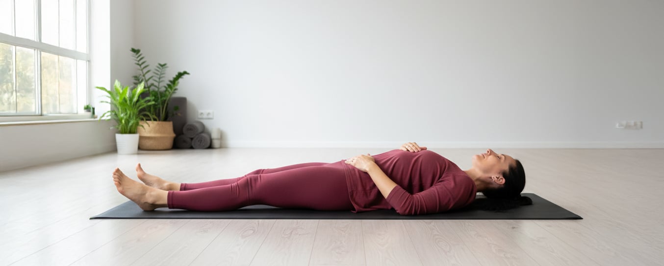 Mette laying in savasana pose resting on yoga mat on a light hard wood floor