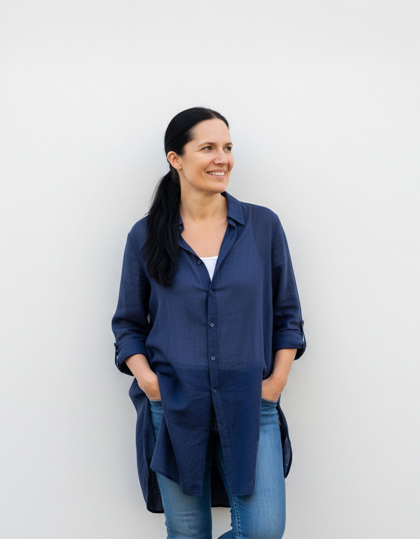 Mette resting standing smiling against a white wall