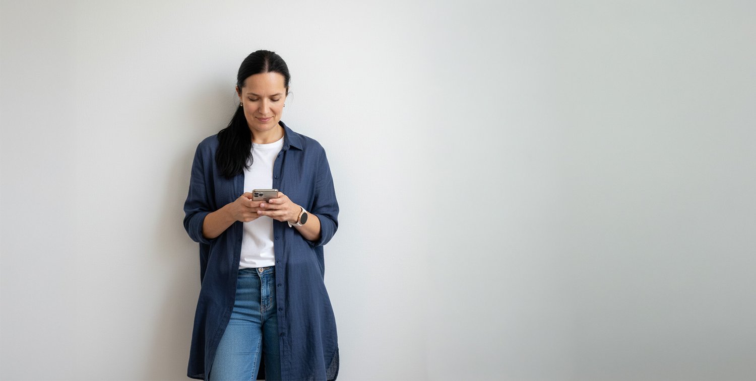Mette smiling standing against a white wall texting on her phone to a coaching client