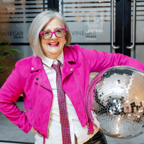 LinkedIn trainer Esther Partridge-Warner smiling in a pink jacket with disco ball, representing visibility and confidence.