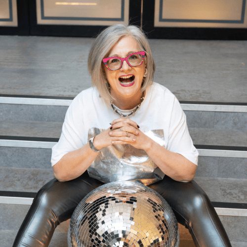 LinkedIn trainer Esther Partridge-Warner sitting on steps with disco ball, symbolising visibility and fun in business.