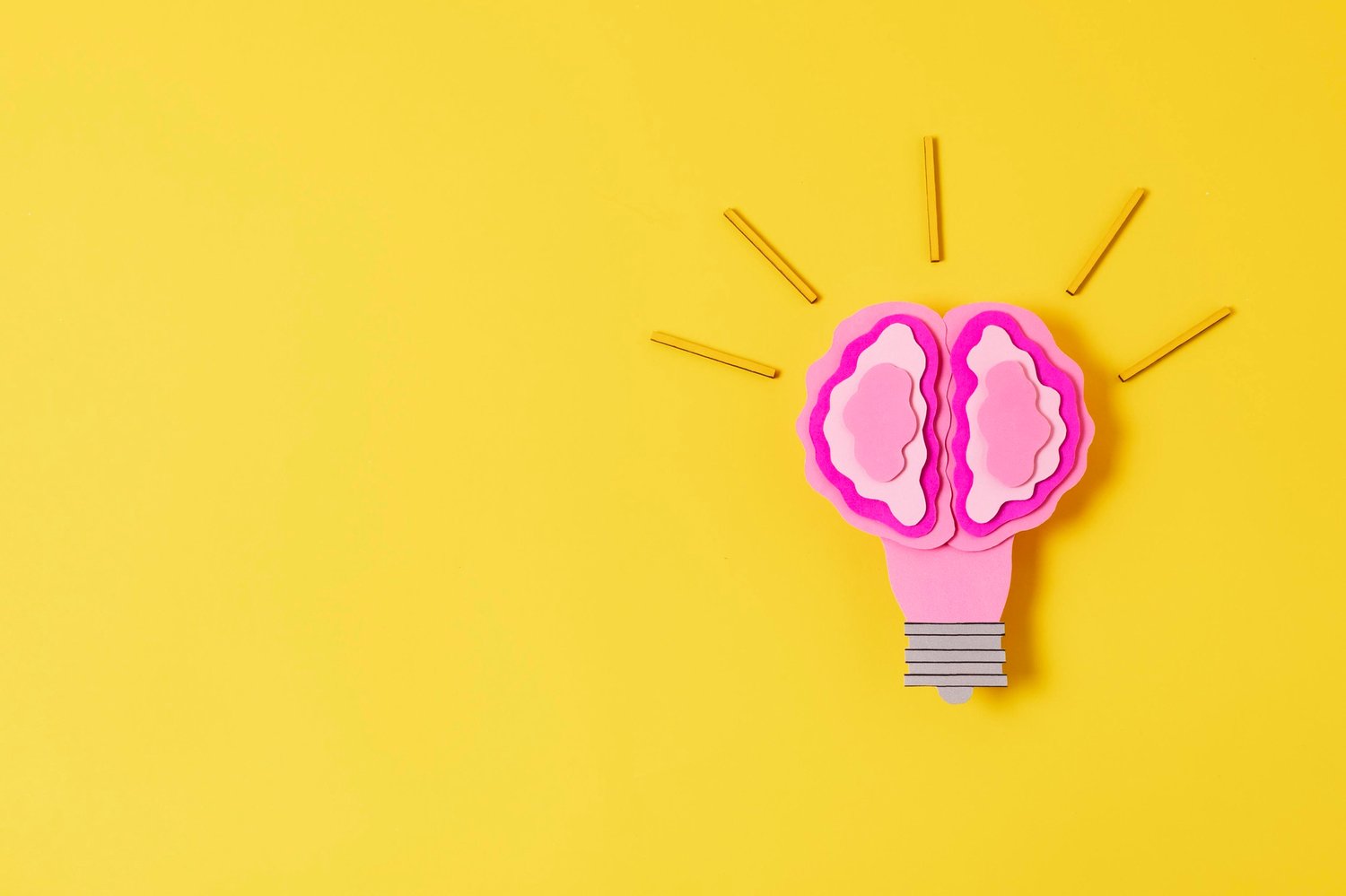 Bombilla rosa con forma de cerebro sobre fondo amarillo, simbolizando la unión entre creatividad e inteligencia estratégica.