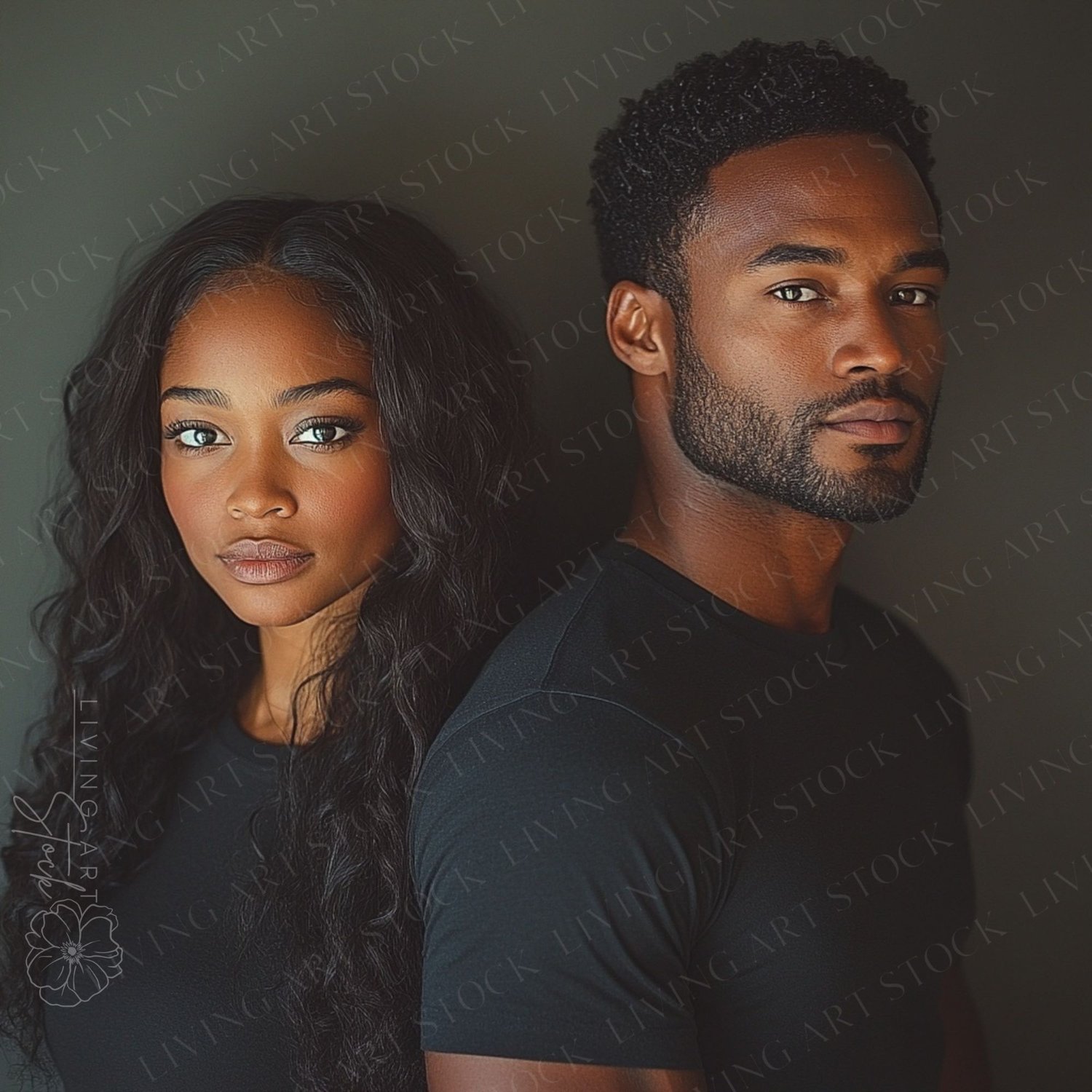 A dramatic and compelling studio portrait of a serious and attractive Black couple standing back-to-back. The woman, with long, wavy dark hair and striking eyes, stands on the left. The man, with a neat beard and short, textured hair, stands on the right.