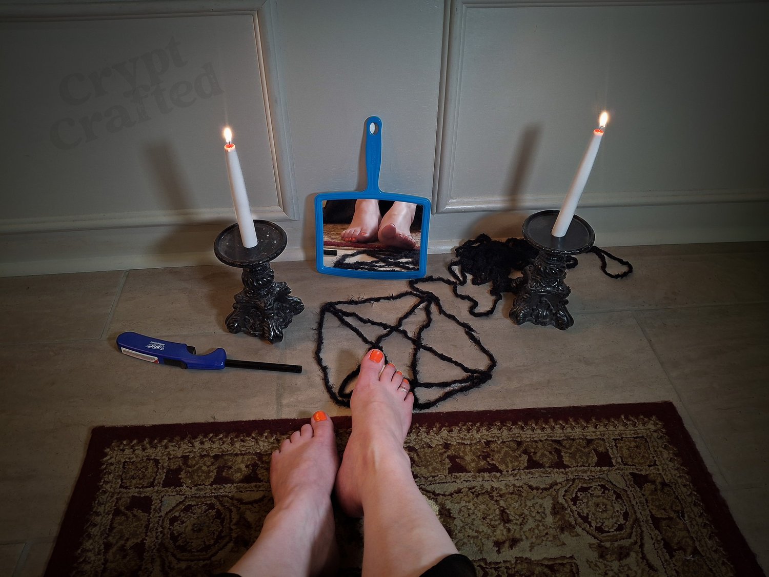 pale feet with bright orange nail polish resting on a bathroom area rug before a blue hand mirror surrounded by an alter