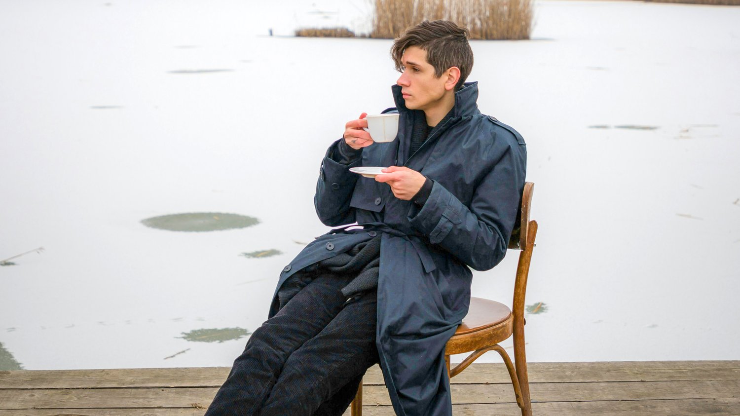 A person in a dark coat sits at the edge of a frozen lake, holding a cup and saucer, reflecting the calm focus and quiet attention described in The Creative Guide’s “Protecting Flow.”