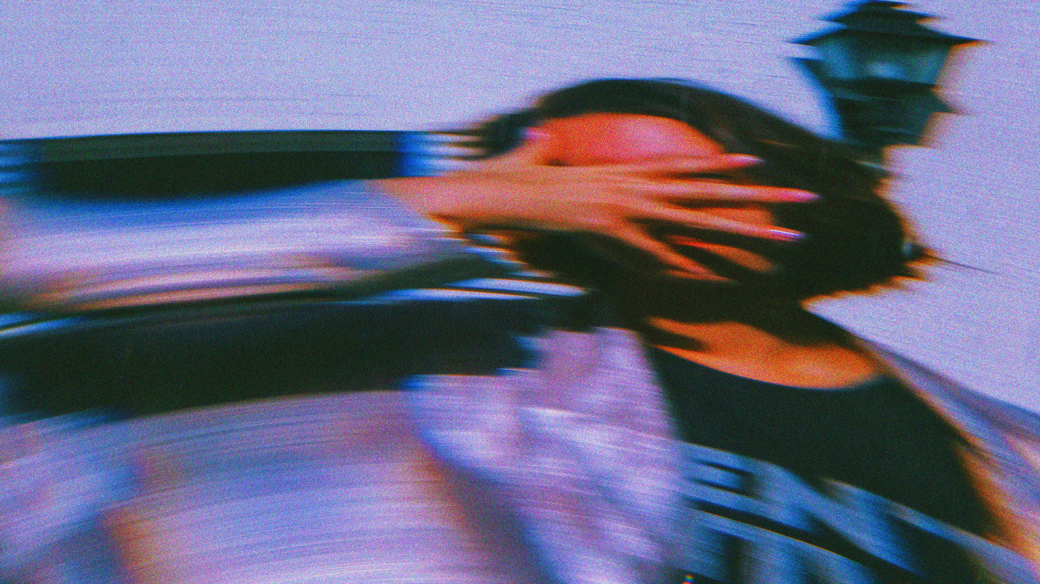A blurred, motion-streaked photograph of a person shielding their face with one hand, surrounded by vivid purples and blues, symbolizing how perception distorts reality in The Creative Guide’s “When Perception Gets Ahead of Reality.”