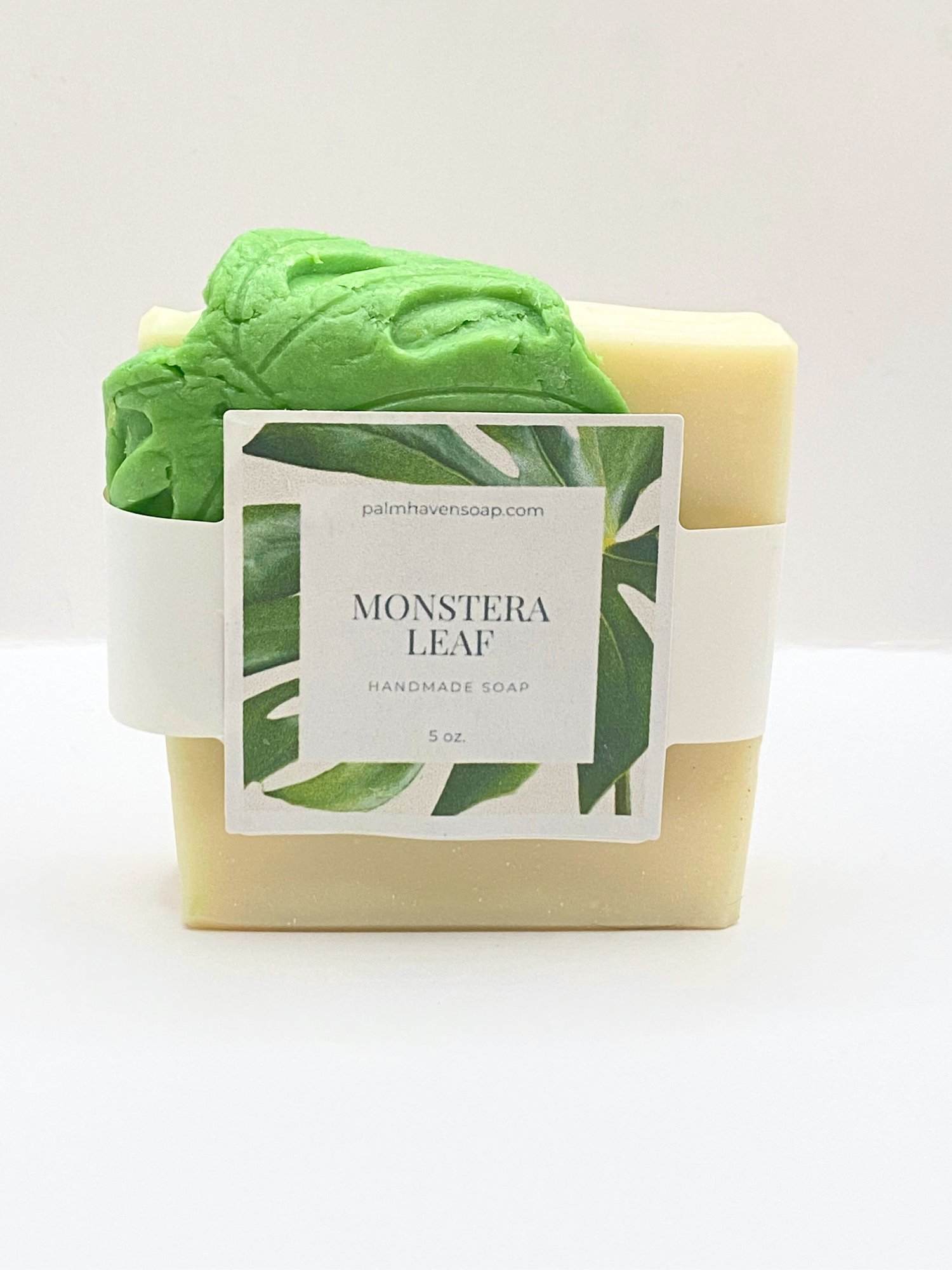 Handmade white soap draped with a green soap monstera leaf