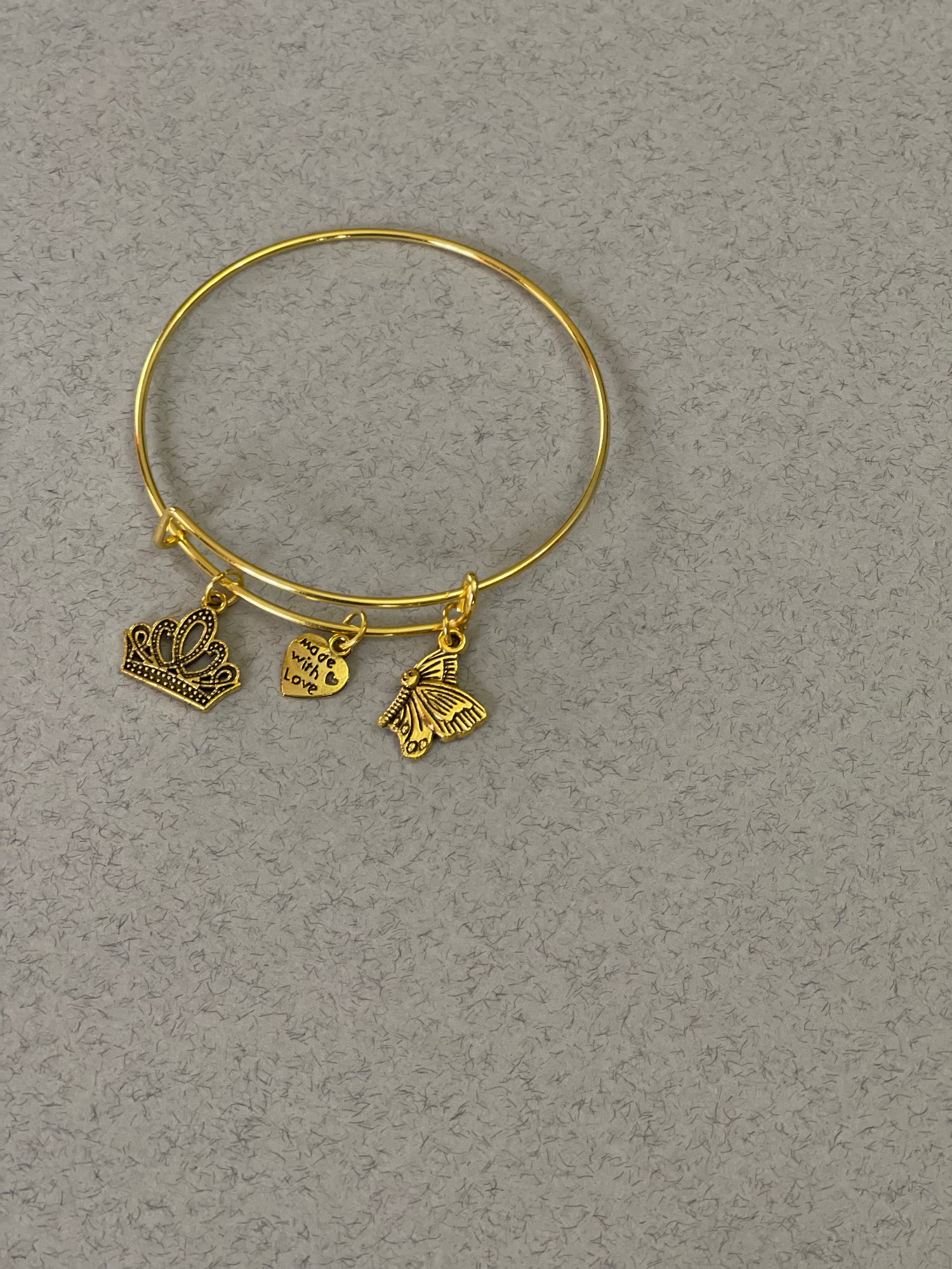This item is a gold-tone, expandable bangle bracelet featuring charms that represent the amor of God, as outline in Ephesians Chapter 6. The charm are designs to move freely along the bracelet. This bangle is crafted to expand, allowing it to fit a variet