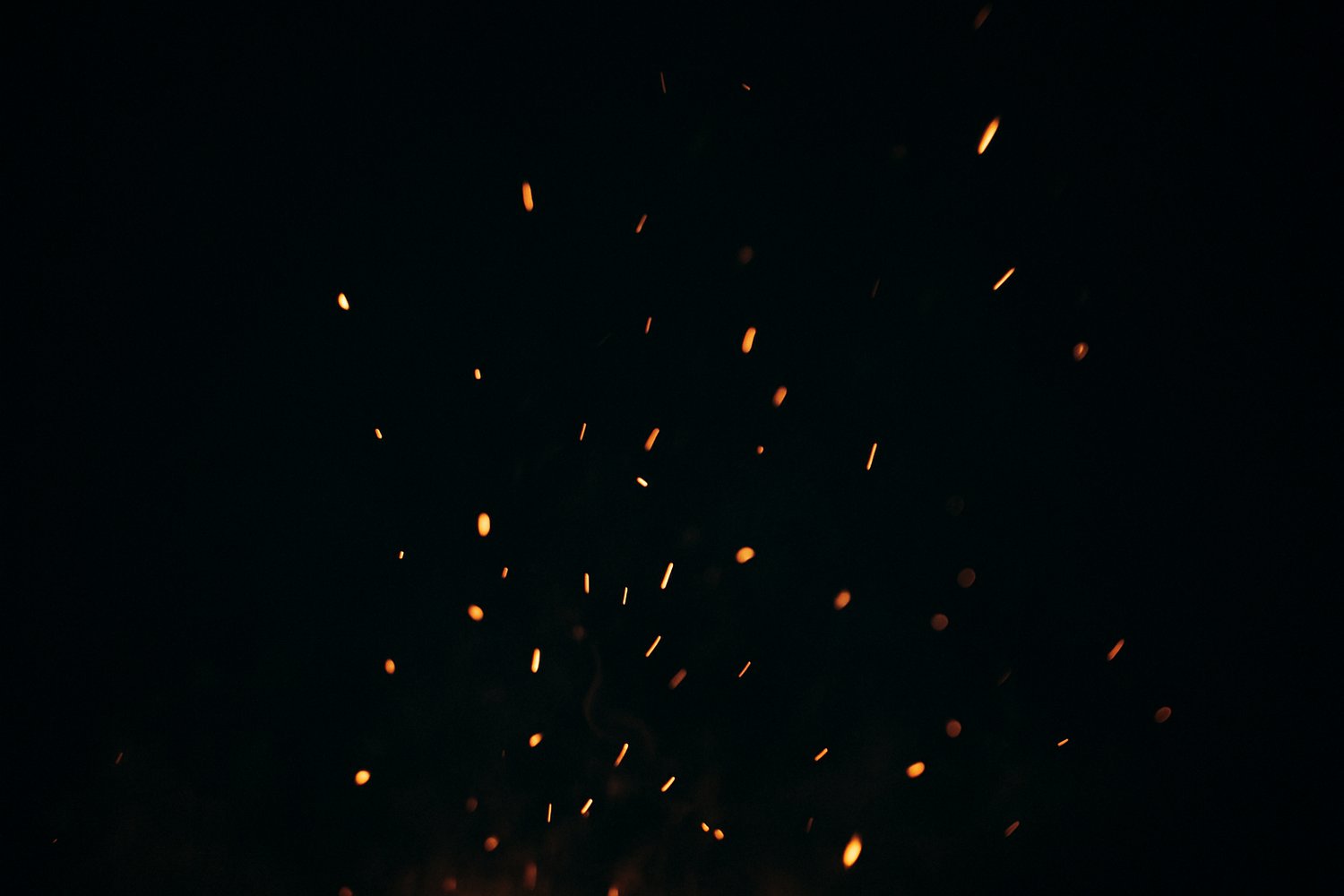 Close-up of glowing orange embers rising against a dark night background, symbolizing fire, burning traditions, and the haunting atmosphere of Bonfire Night and Guy Fawkes effigy rituals.