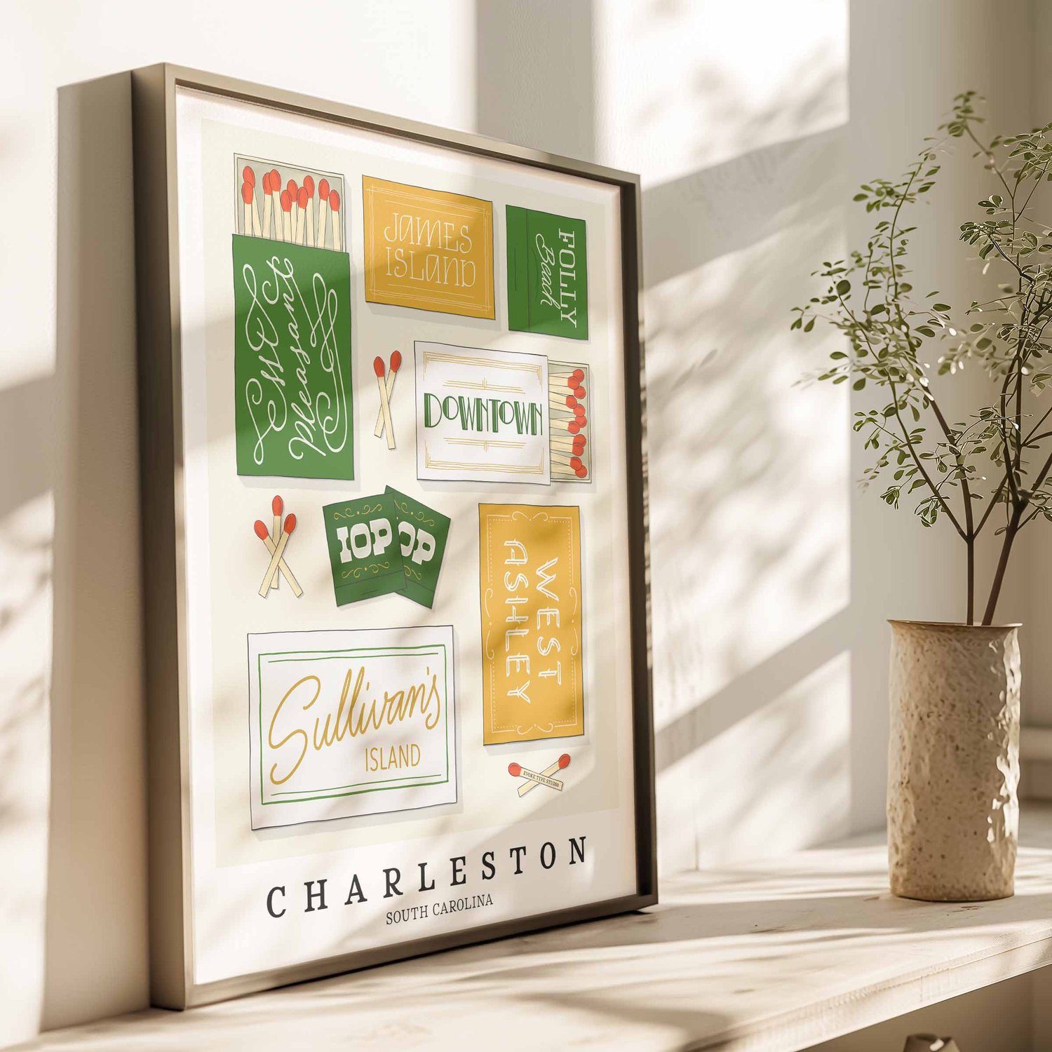 A framed picture of Charleston, South Carolina neighborhoods drawn in various lettering styles on matchboxes. Artwork has a green, yellow and white color scheme.