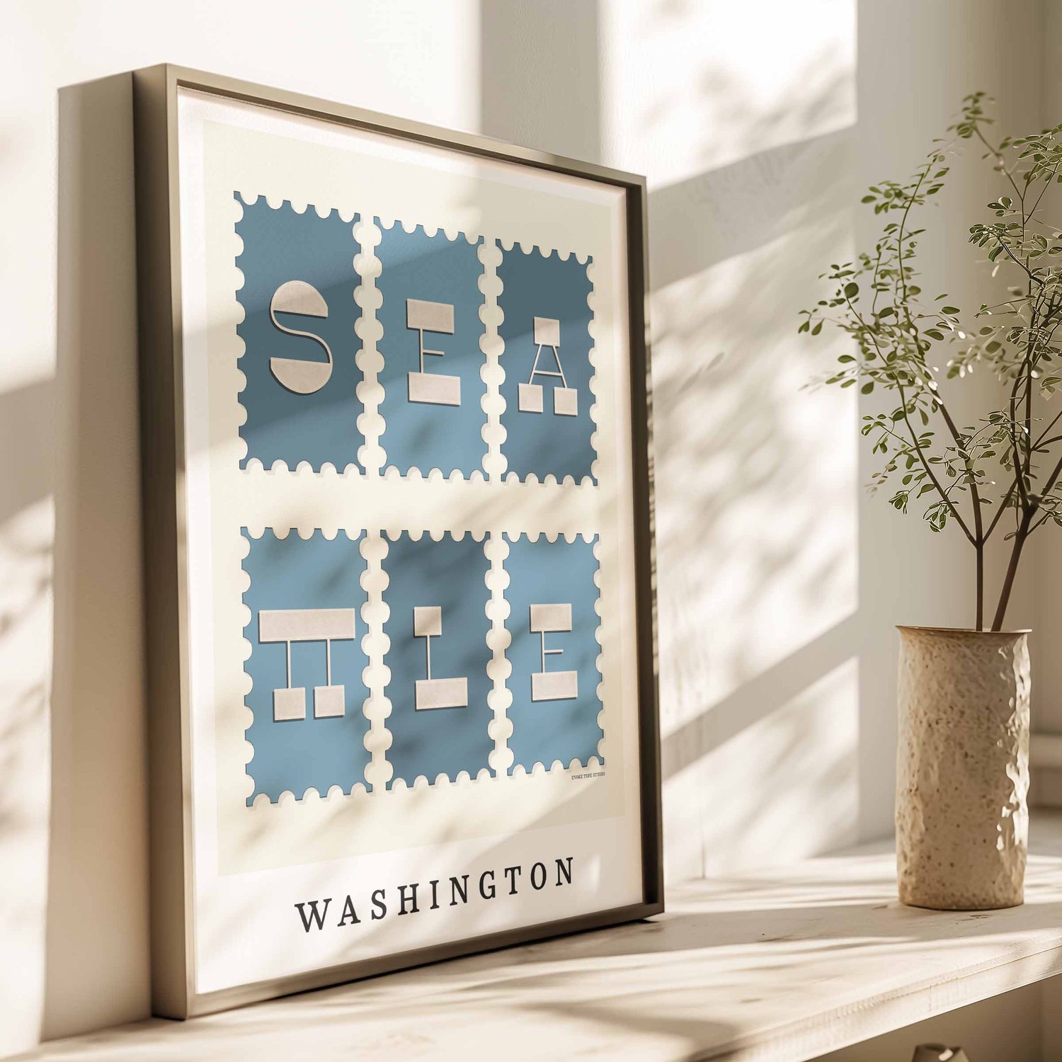 A framed picture of postage stamps featuring Seattle, Washington drawn in a unique lettering style. Artwork has a blue and beige color scheme