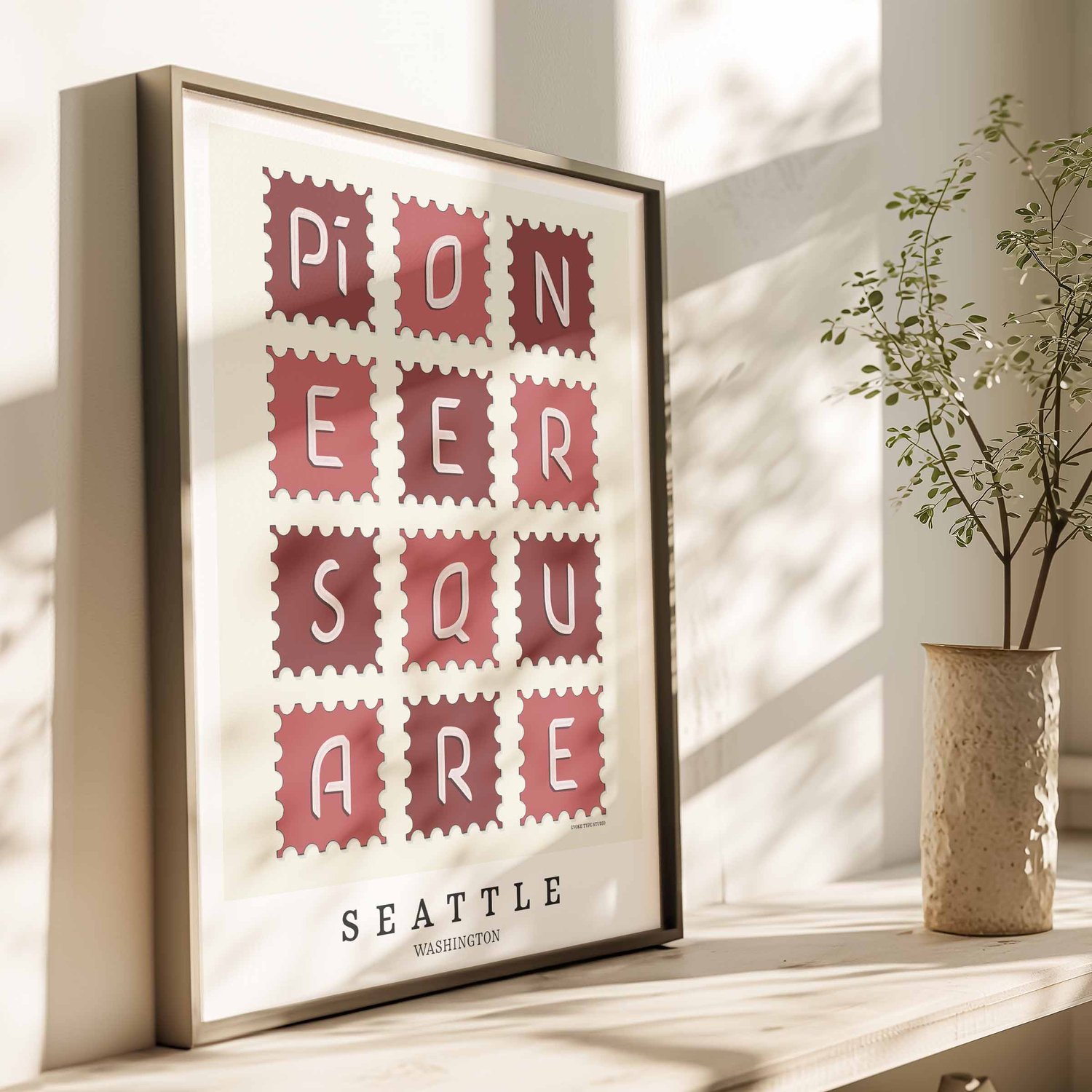A framed picture of postage stamps featuring the Pioneer Square neighborhood in Seattle, Washington drawn in a unique lettering style. Artwork has a red and white color scheme