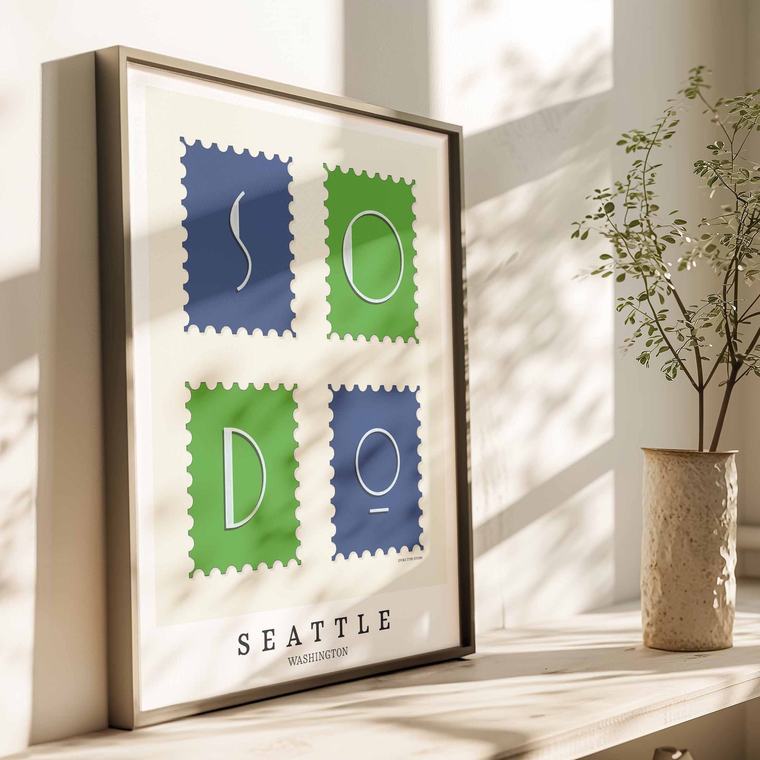 A framed picture of postage stamps featuring the SoDo neighborhood in Seattle, Washington drawn in a unique lettering style. Artwork has a bright blue and green color scheme