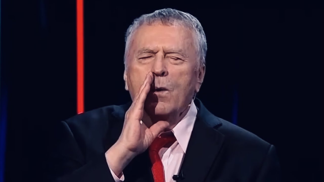 A dramatic still from a Russian political talk show showing an elderly male speaker in a suit and red tie gesturing toward his mouth while making a howl-like expression, referencing wolves howling during an intense on-air monologue on a live TV broadcast.