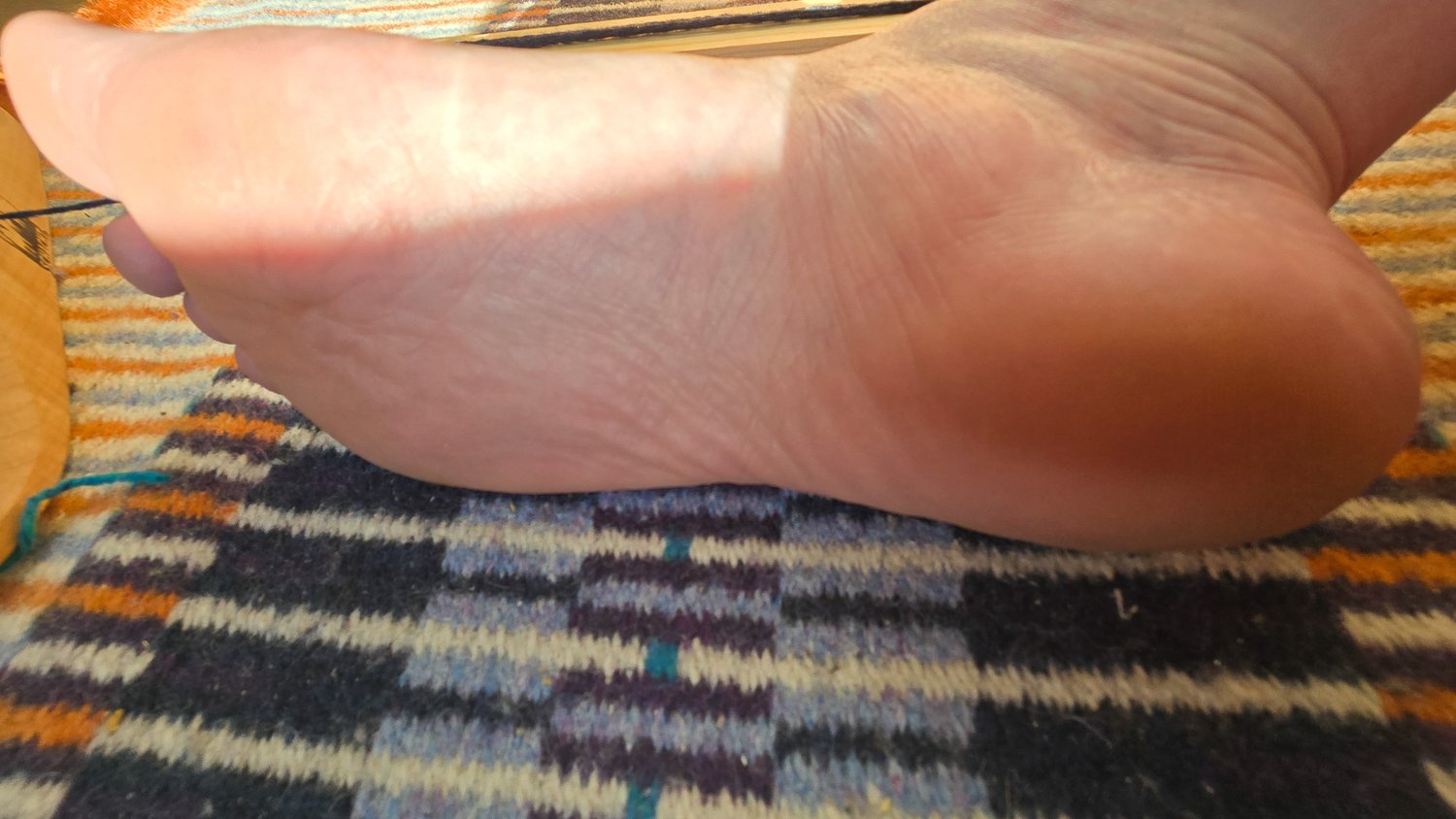 close up of foot resting on it's side sole exposed to viewer on a wool krokbradg rug