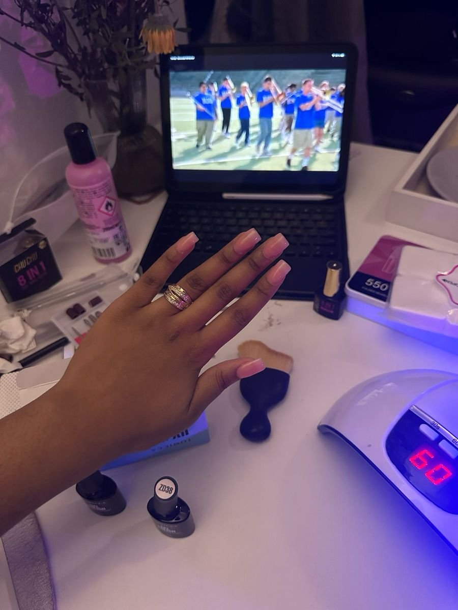 Nail technician applying intricate nail art on a client’s hands in a bright, organized nail studio, demonstrating professional skill and precision.