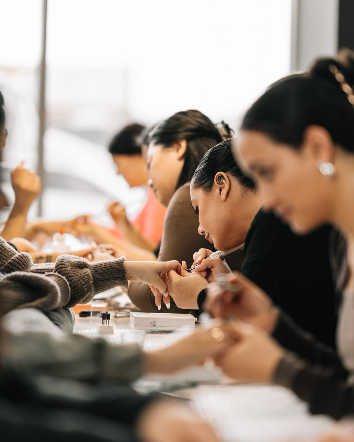 Professional nail technician applying intricate nail art on a client’s hands in a modern, organized nail studio, demonstrating precision and skill