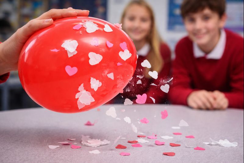 Red balloon attracting tissue paper and confetti through static electricity with students blurred in back