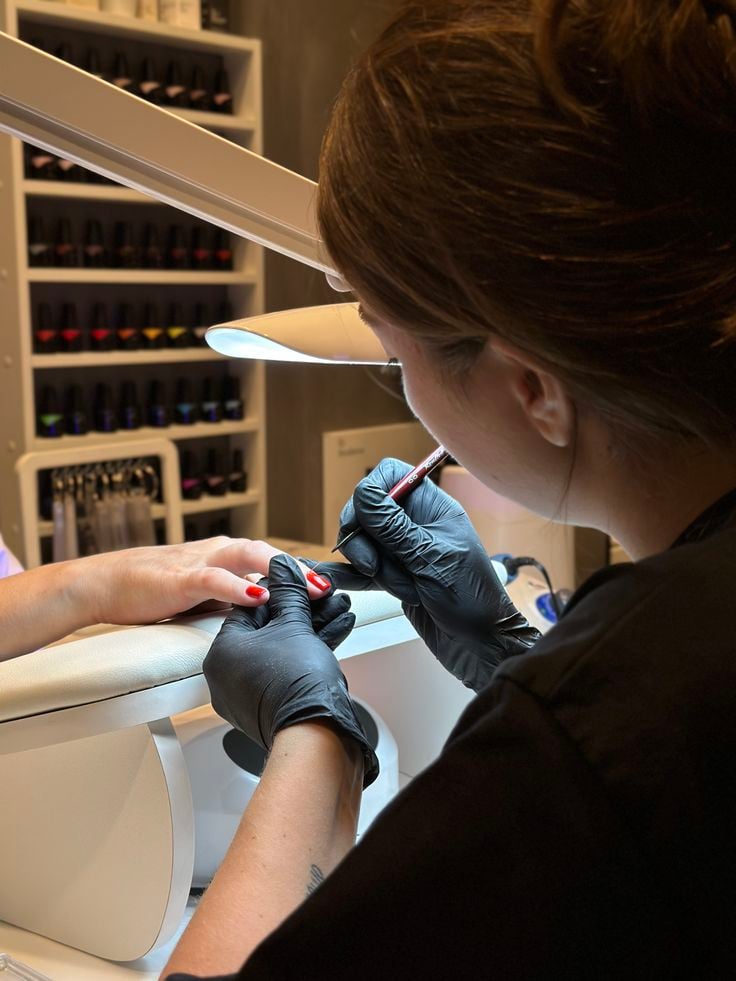 Nail technician applying intricate nail art on a client’s nails in a modern, organized nail studio, demonstrating professional skill and precision.
