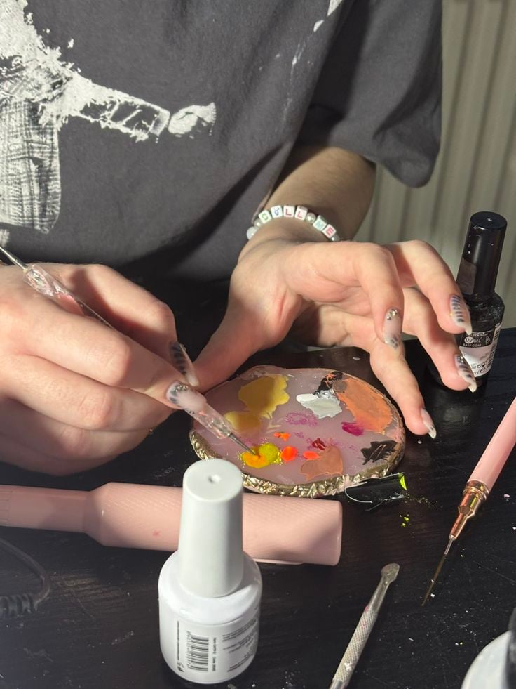 Professional nail technician painting detailed nail art on a client’s nails in a modern, organized studio, demonstrating skill and precision.