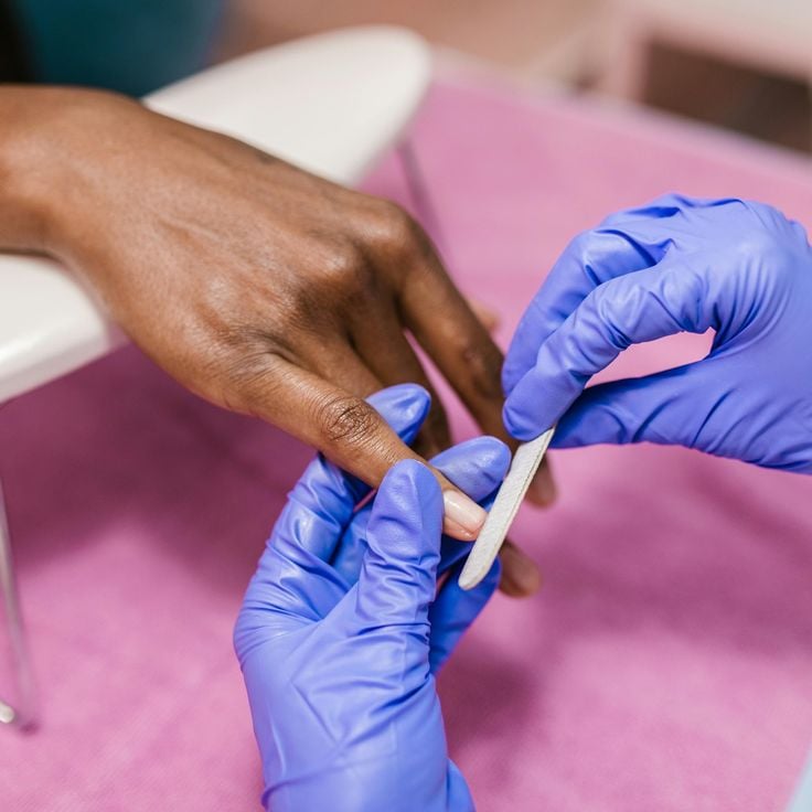 Nail technician smiling and providing a manicure to a client in a clean, modern studio, demonstrating client care and loyalty building.